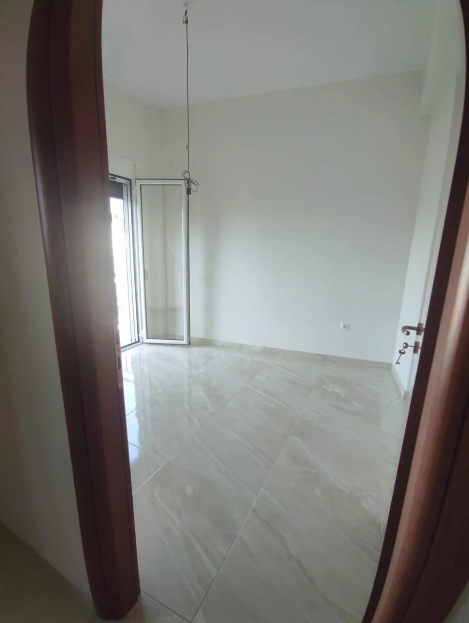 Empty room with white walls, marble tile floor, and a large window with a sliding door