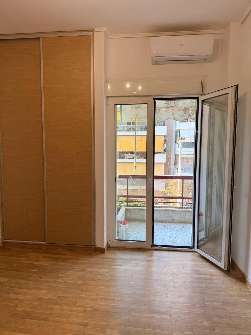 Empty room with wooden flooring, a large sliding glass door leading to a balcony, and built-in closet with wooden sliding doors.