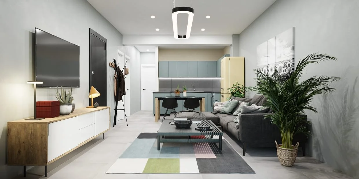Living room with gray sofa, coffee table, large potted plant, wall art, flat-screen TV, and open kitchen with blue cabinets in the background.