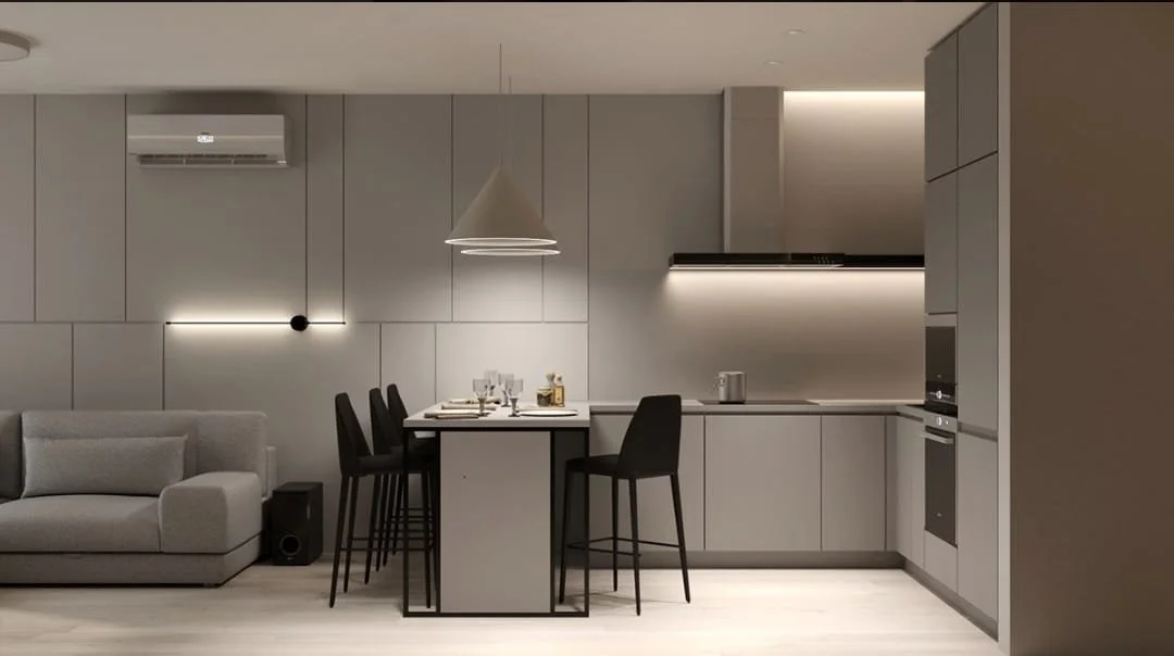Modern, minimalistic kitchen and living room with gray cabinetry, black chairs around a kitchen island, a gray sofa, and soft lighting.