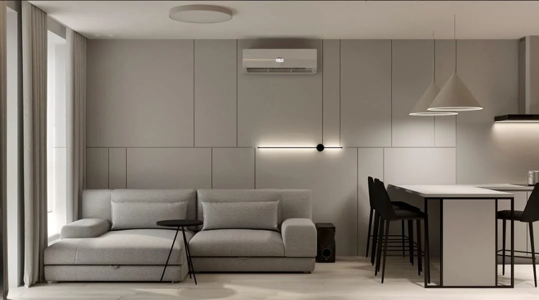 Modern living room with a gray sofa, black side table, wall-mounted light, and a dining area with a high table and four bar stools. Neutral color palette.