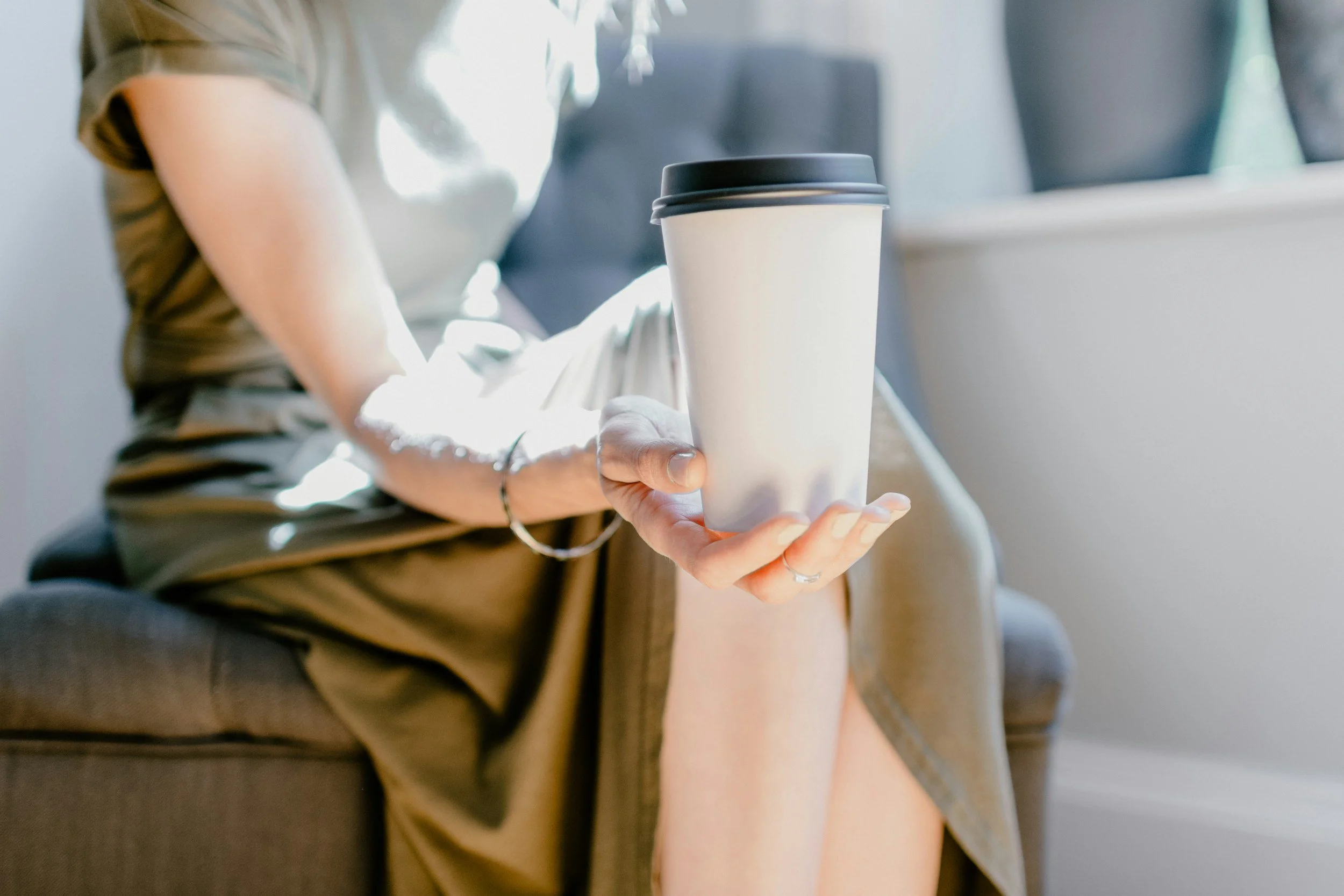 Person sitting on a chair holding a takeout coffee cup.