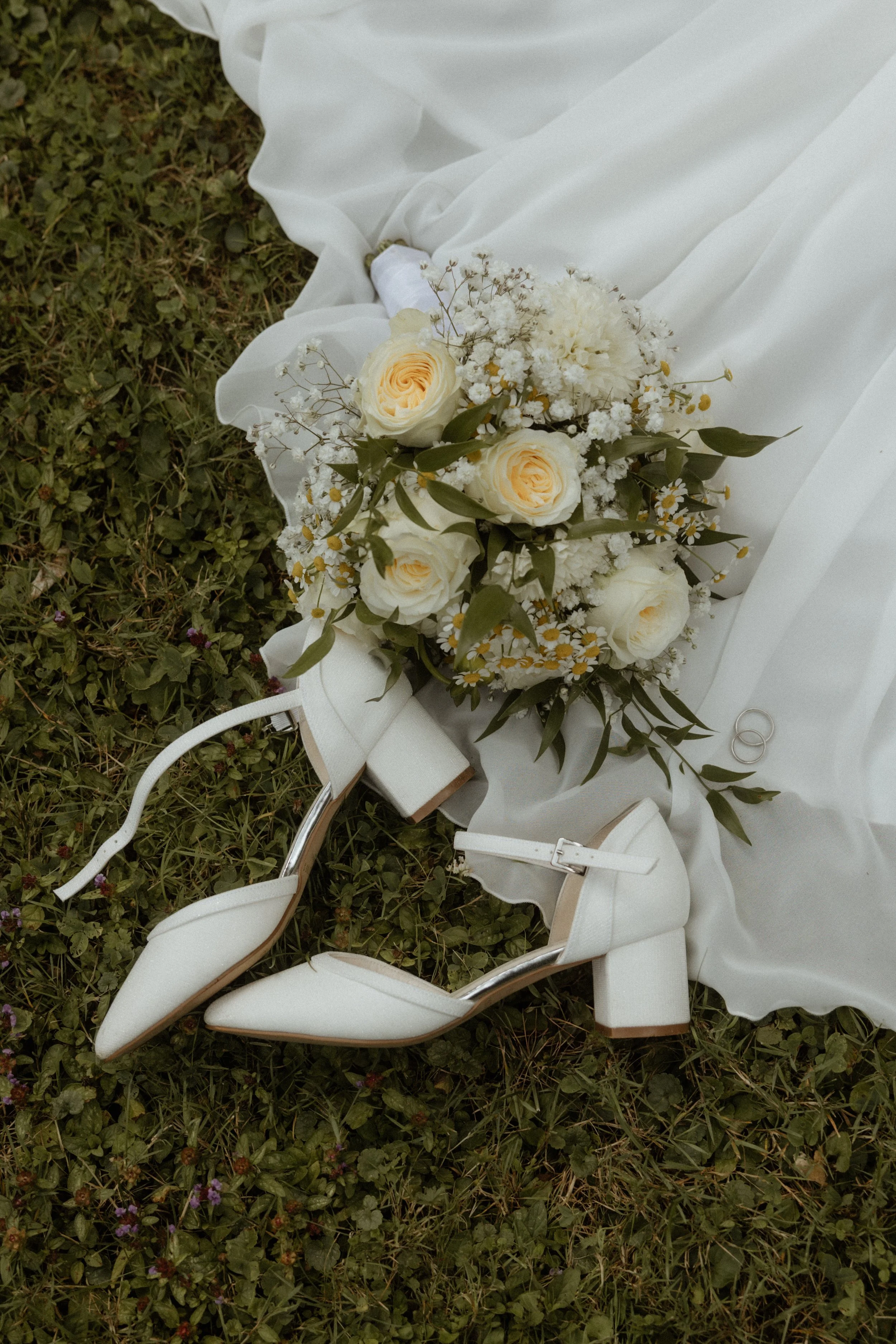 Hochzeitsblumen, weiße High Heels und Eheringe auf Rasen. Flatylay-Fotografie von Pia Lydia Heim.