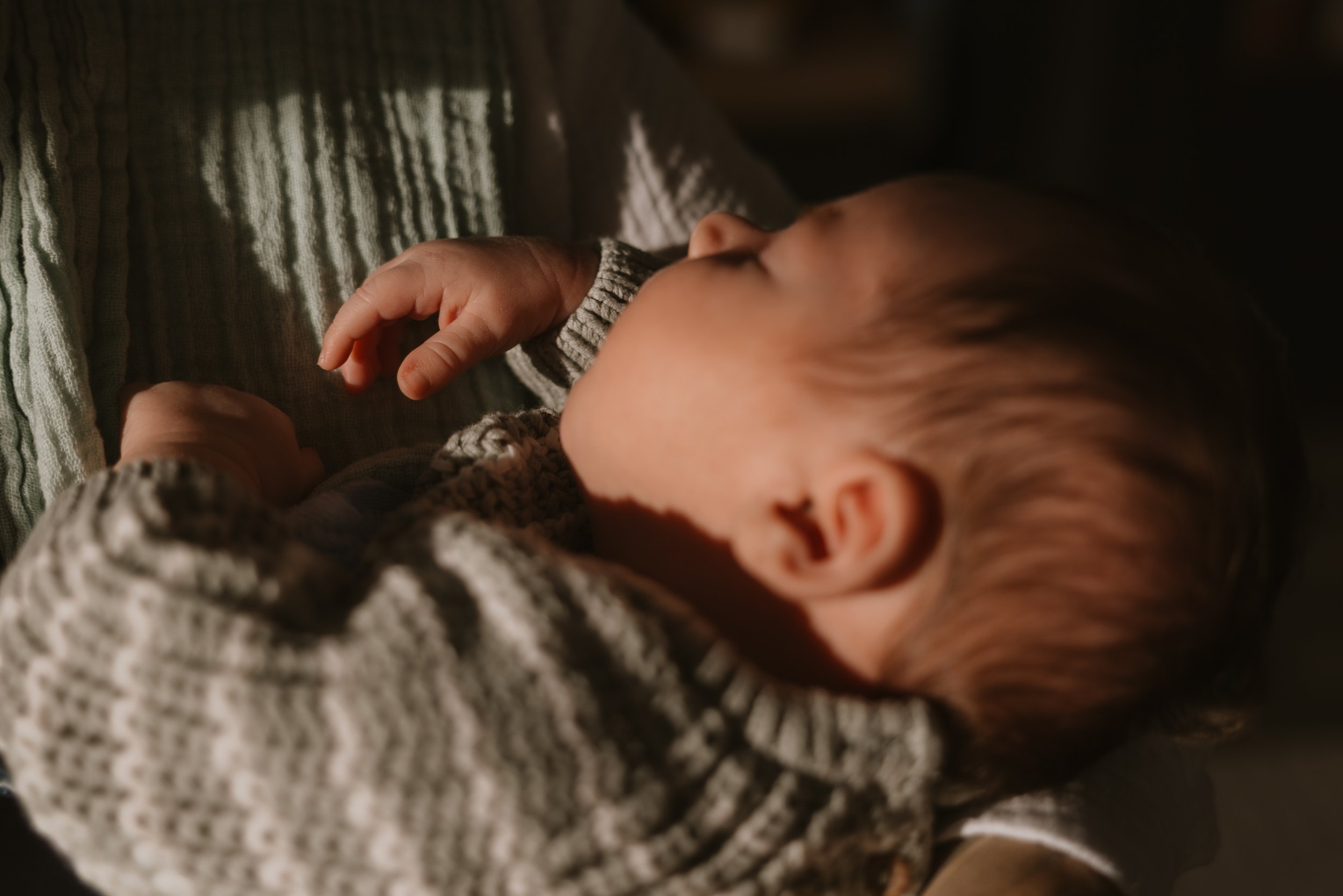 Ein schlafender Baby, das in einem gestreiften Pullover liegt, im Schatten mit warmem Licht.