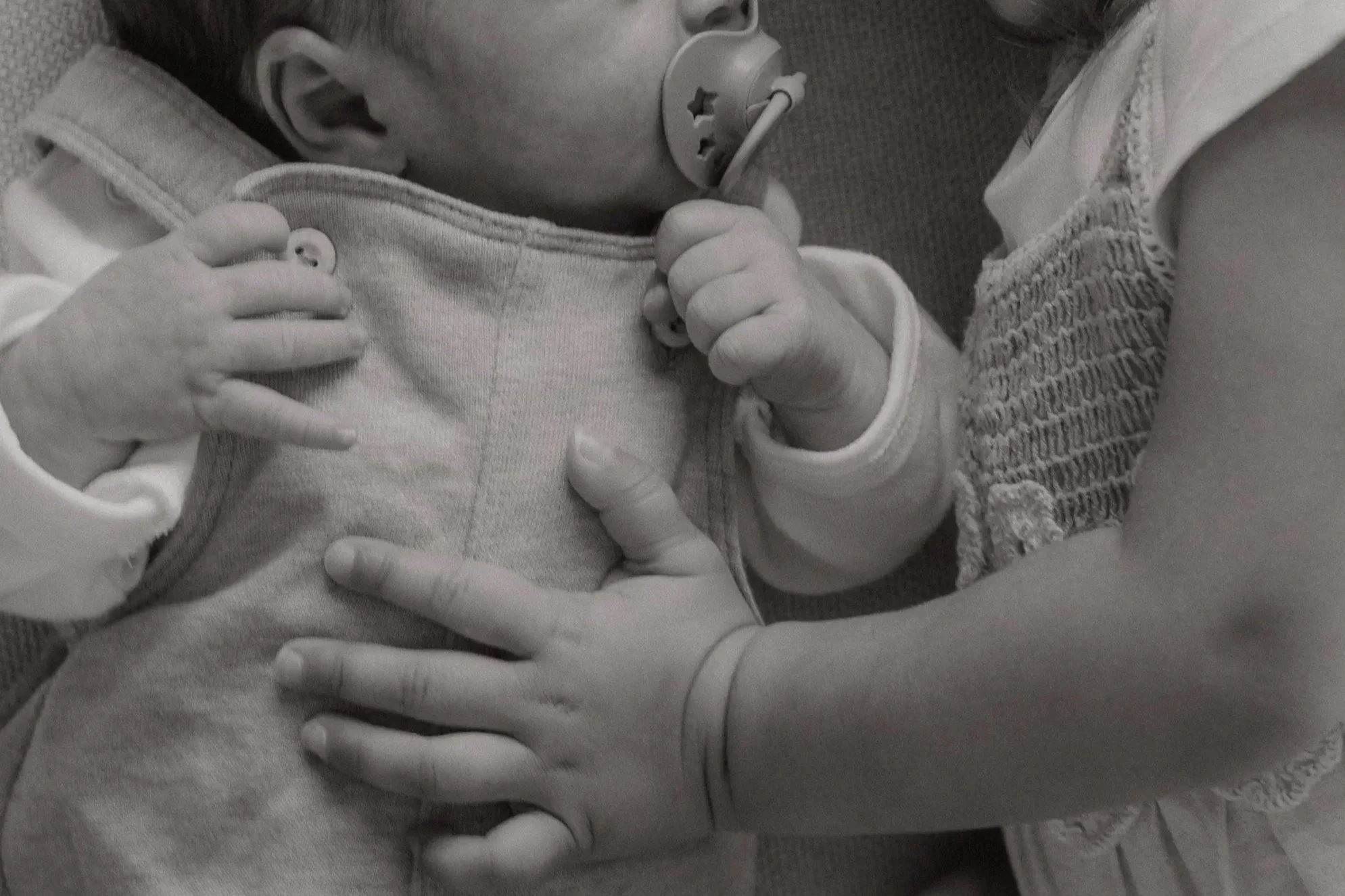 Ein Baby mit Schnuller wird von einer Frau gehalten, die eine Hand auf den Bauch des Babys legt.