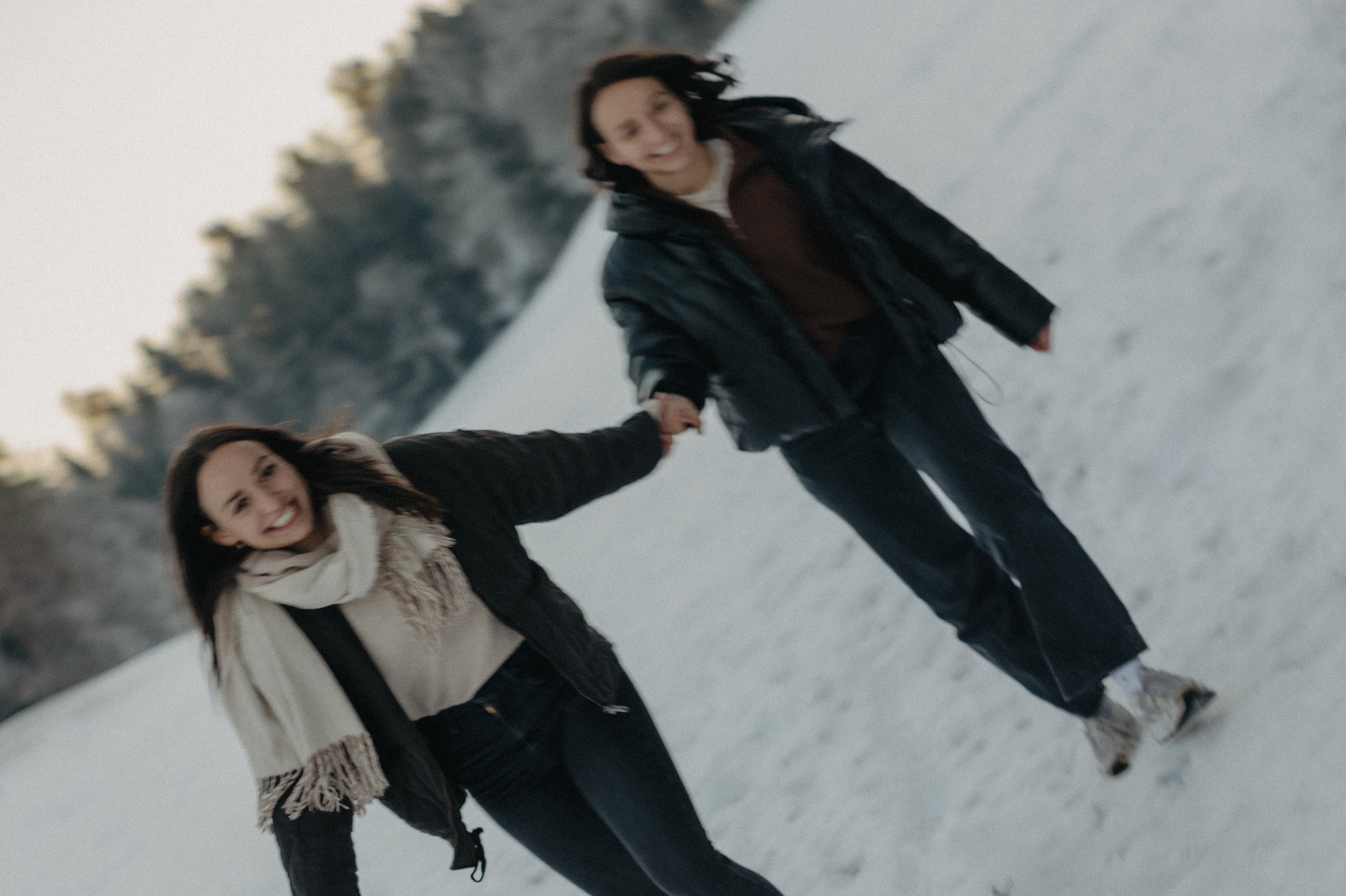 Zwei Schwestern laufen Hand in Hand auf schneebedecktem Weg, lächeln und genießen die Zeit in der Natur. Die Bilder wurden bei einem Familienshooting mit Fotograf Pia Heim gemacht.