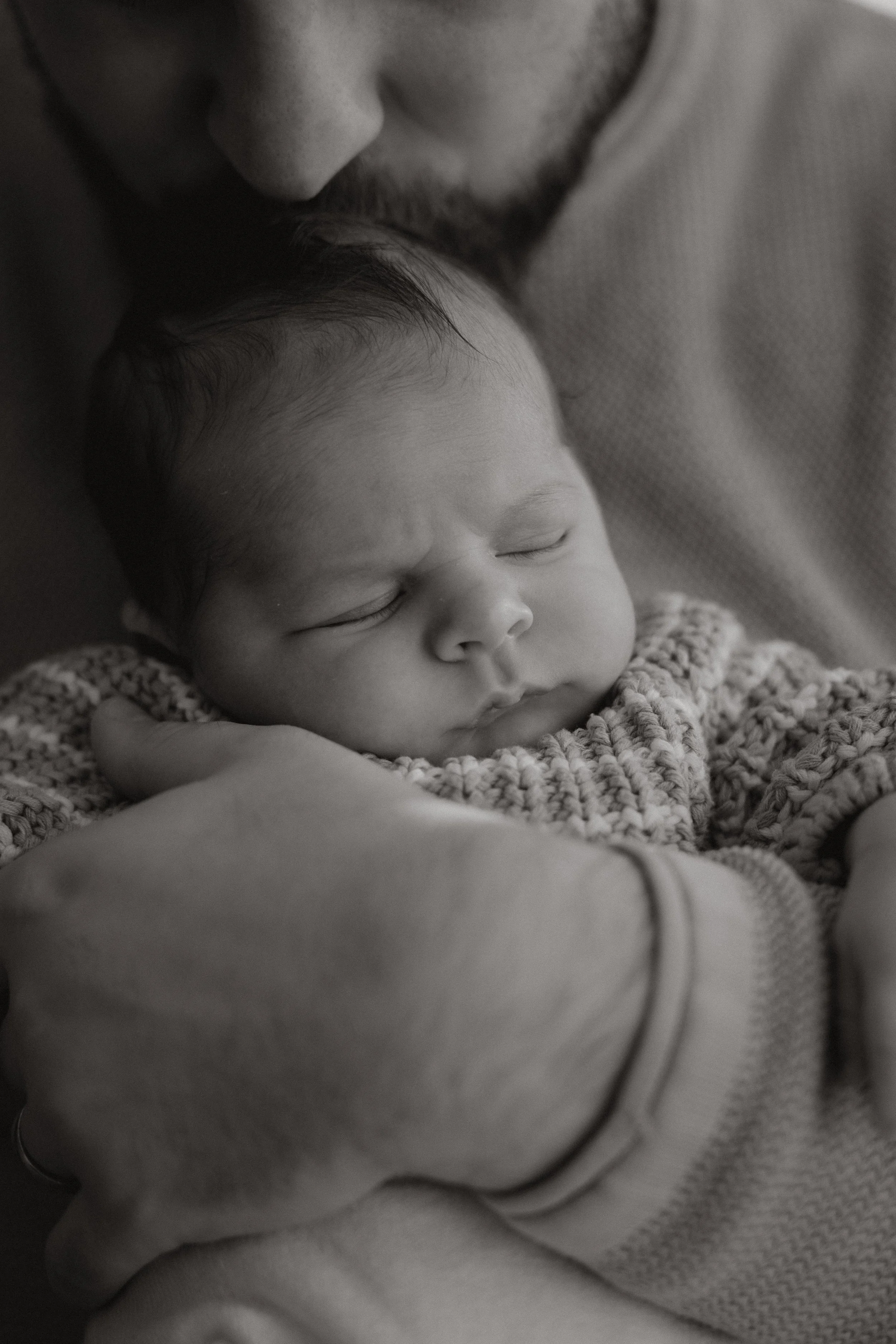 Ein neugeborenes Baby, das schlafend in den Armen eines Erwachsenen liegt, schwarz-weiß aufgenommen.