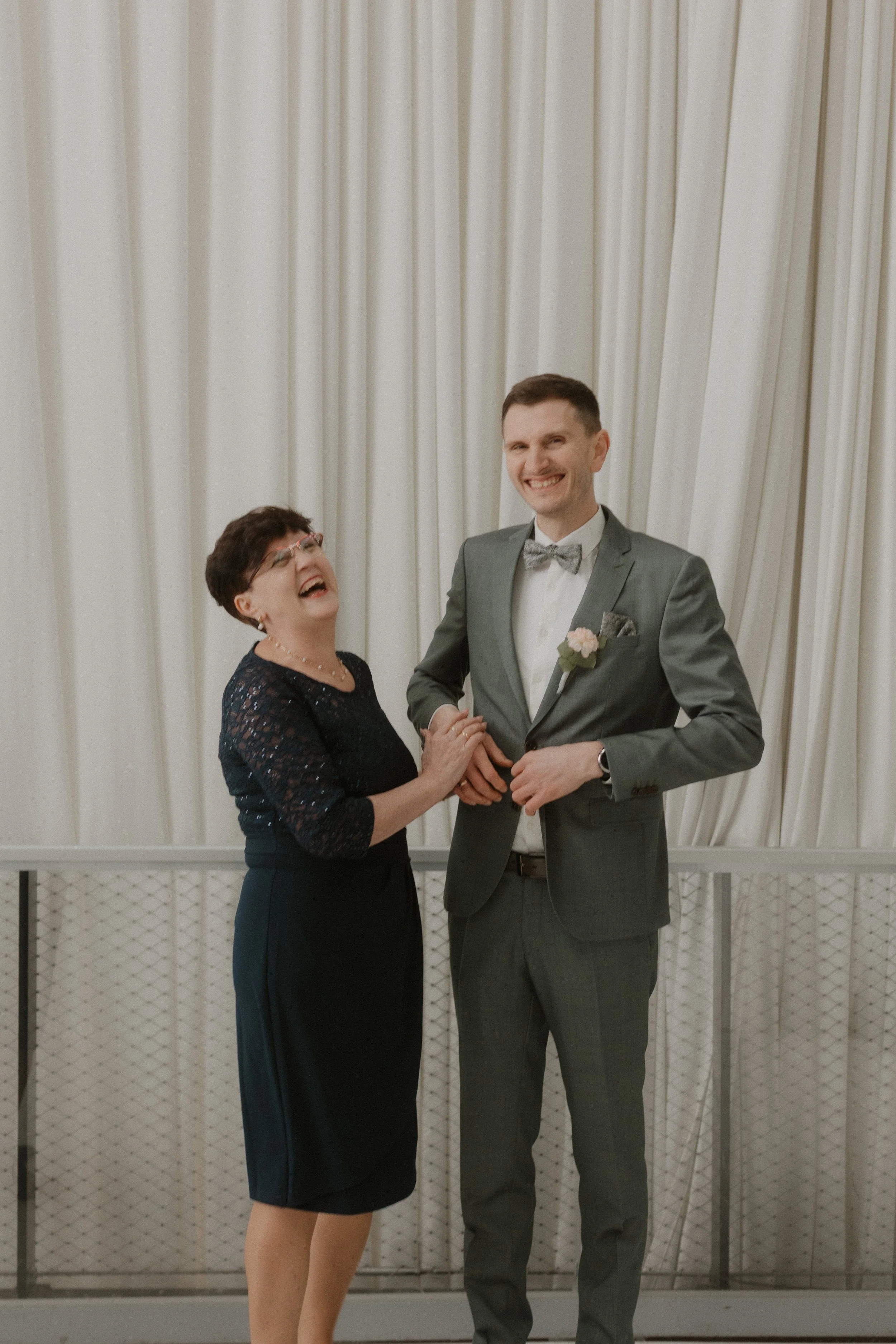 Ein Bräutigam mit seiner Tante fotografiert von Hochzeitsfotograd Pia Lydia Heim bei seiner Hochzeit, lachend vor einem weißen Vorhang in der Bodanwerft, Kressbronn am Bodensee. 