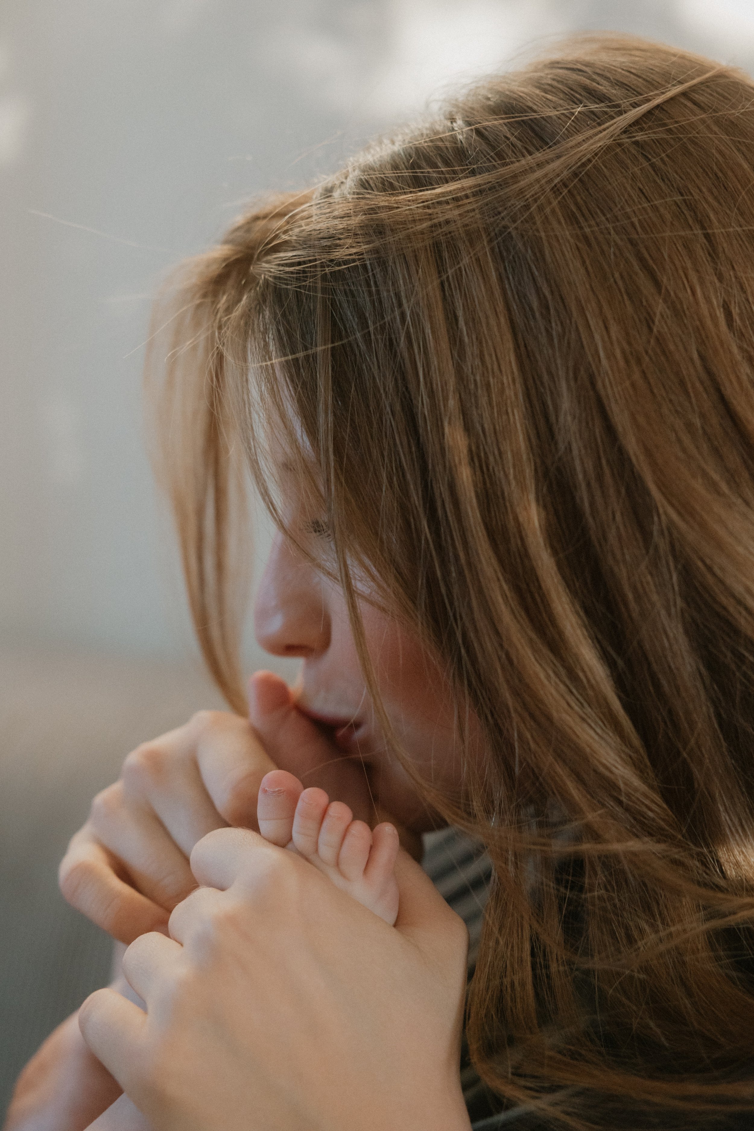 Eine Frau mit langem braunem Haar hält zärtlich die kleine Hand eines Babys. Sie sind in einem ruhigen Moment.