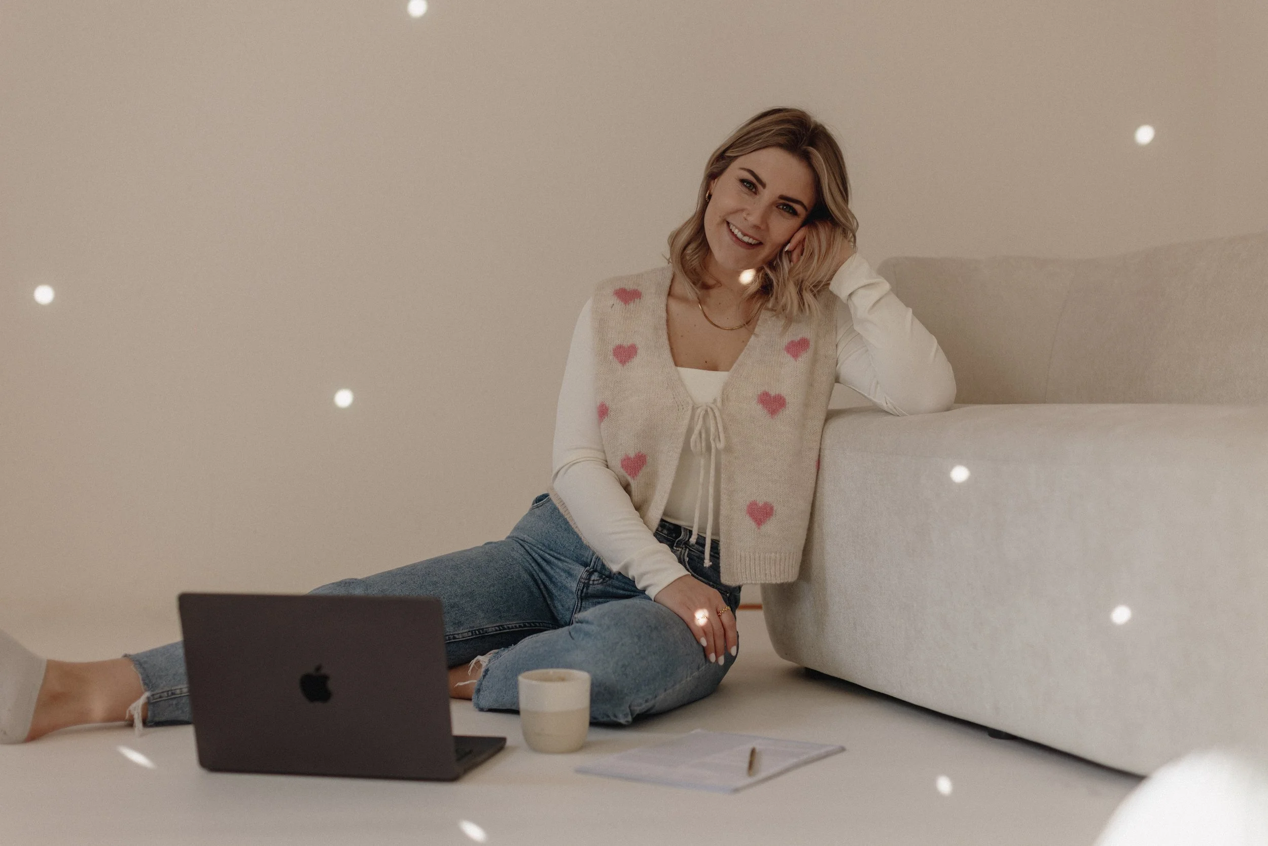 desiistliebezumkind sitzt auf dem Boden neben einem MacBook, einer Kaffeetasse und einem Notizbuch mit Stift. Branding-Shoot mit Pia Heim in einem Studio.
