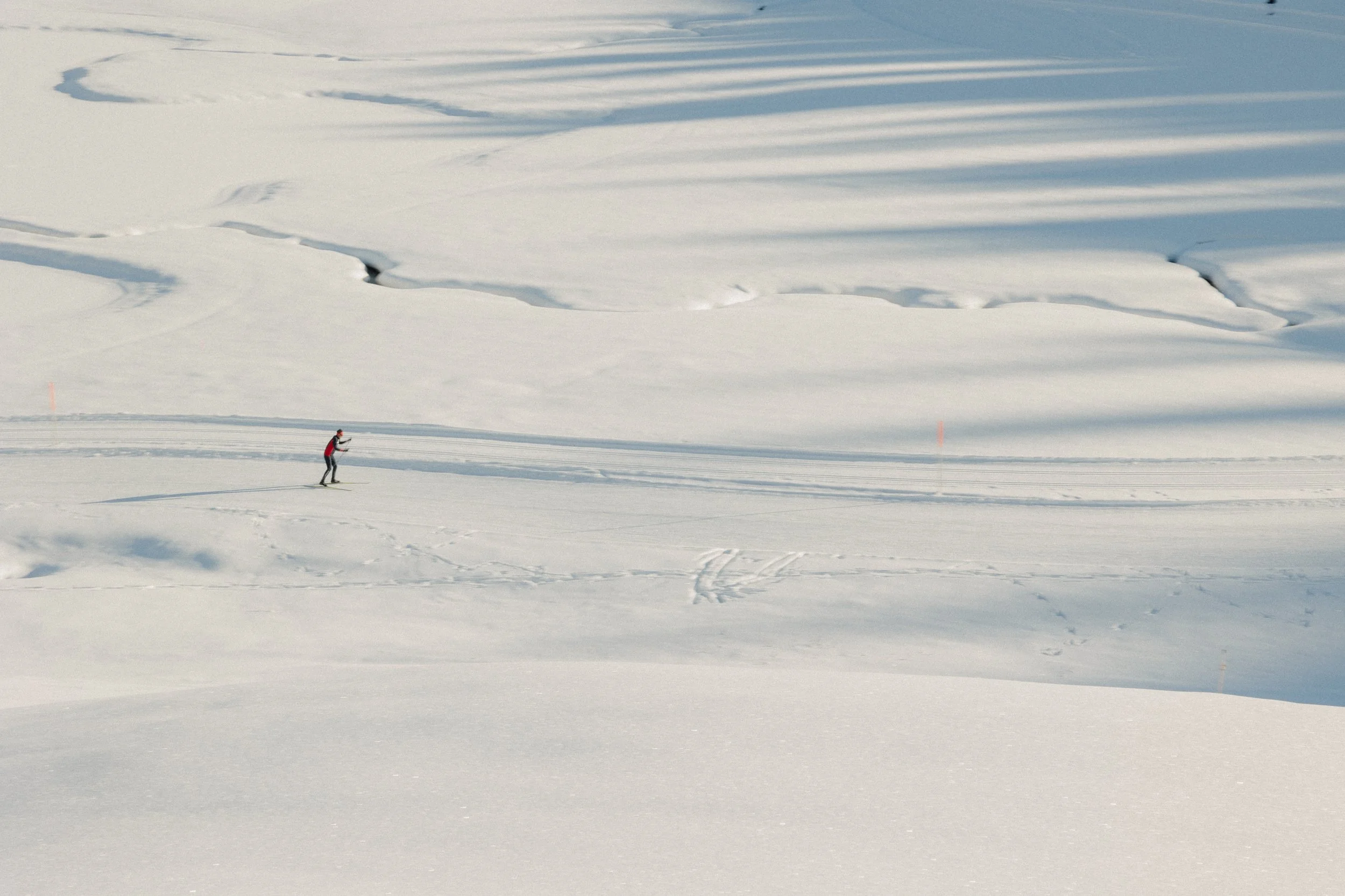 Eine einzelne Person beim Skilanglauf in einer verschneiten, weiten Winterlandschaft. In Österreich, moderne Sportfotografie mit Pia Lydia Hem.