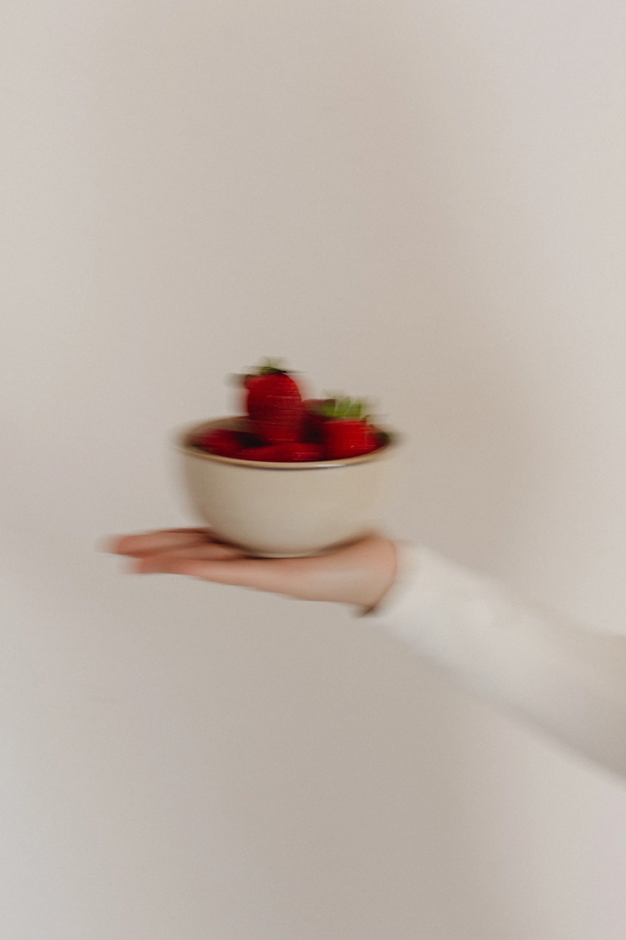 Eine Hand hält eine weiße Schale mit Erdbeeren, die leicht verschwommen ist. Slow Shutter Fotografie.