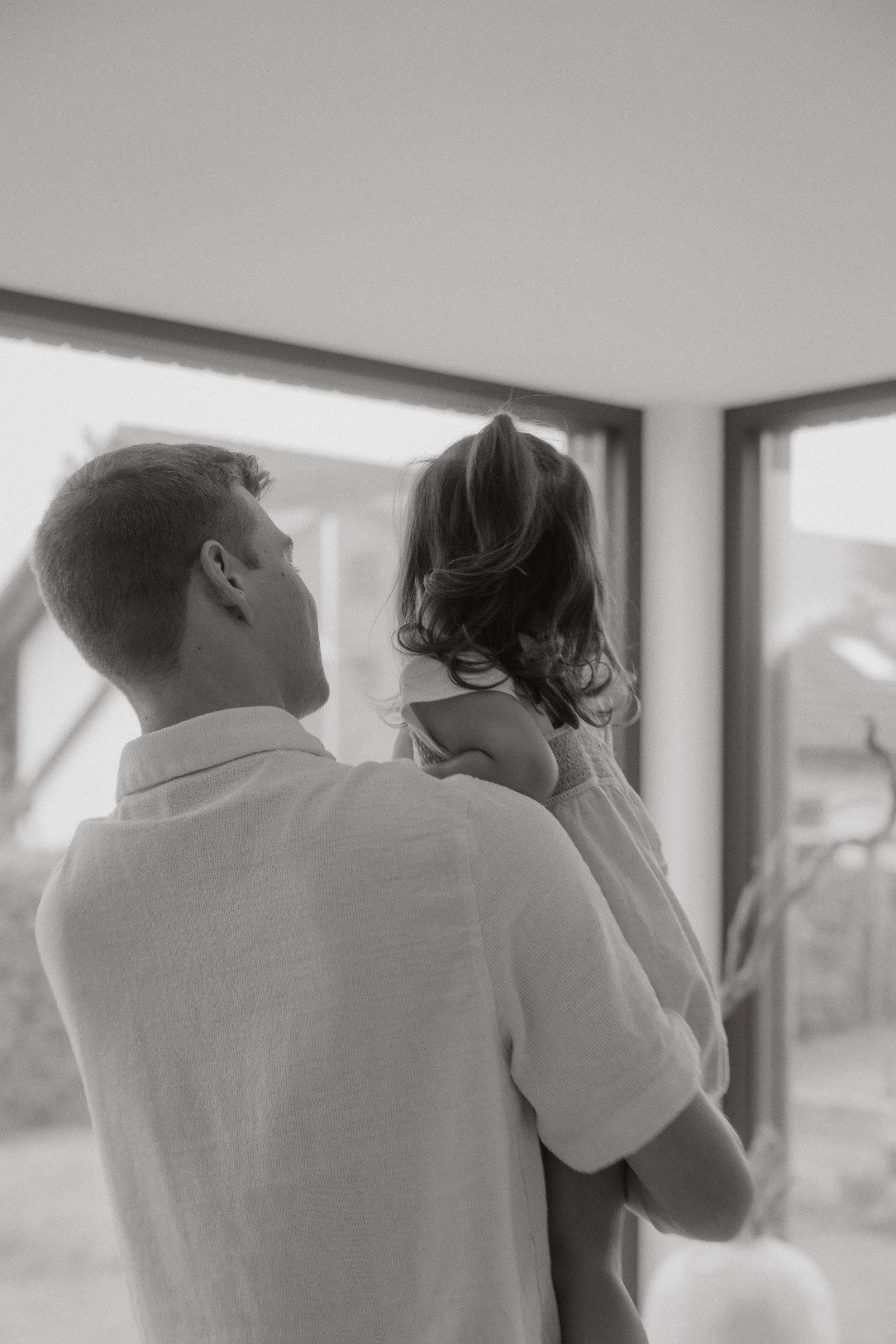Ein Mann trägt ein kleines Mädchen, während sie gemeinsam auf ein großes Fenster schauen.