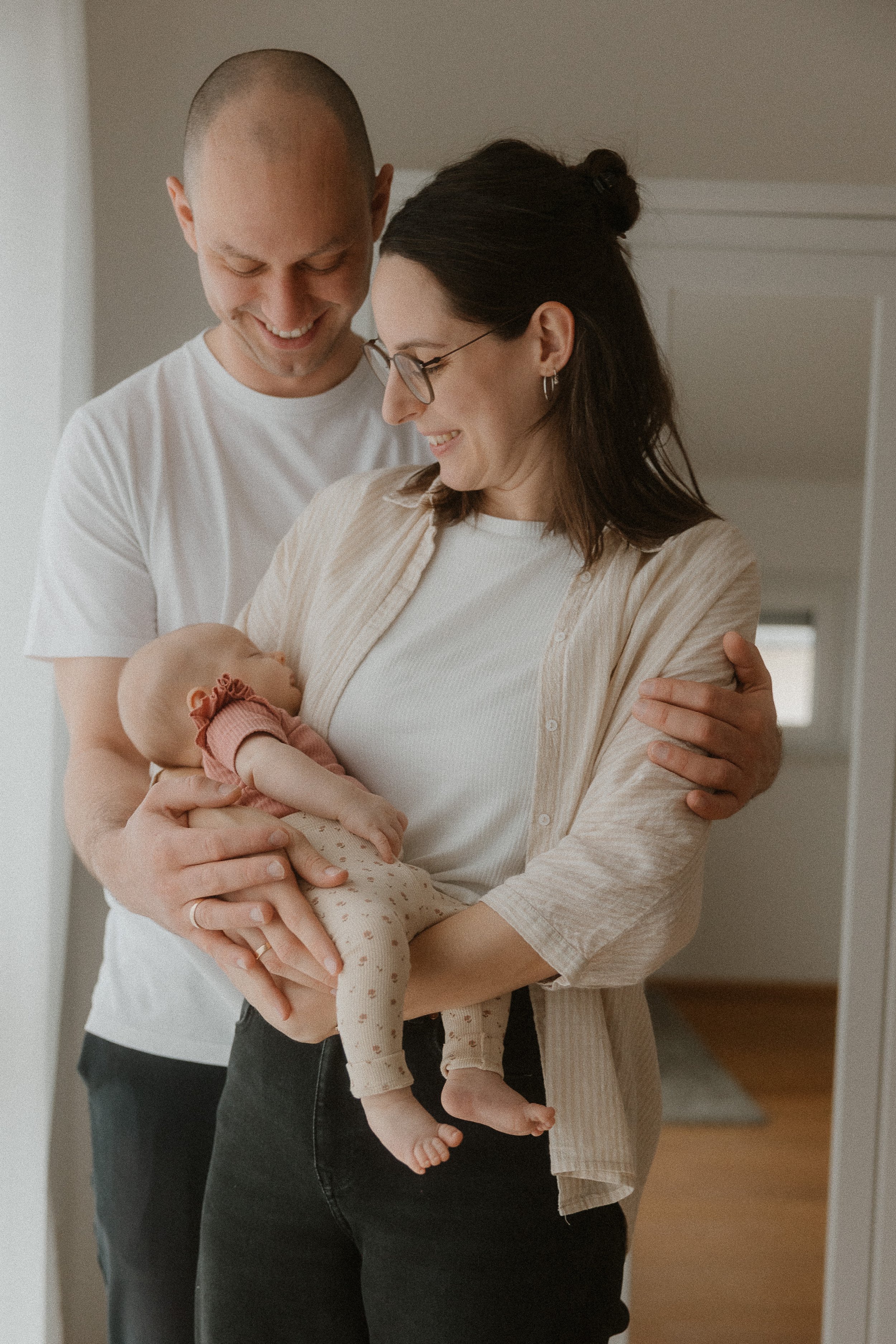 Ein glückliches Paar hält ein neugeborenes Baby in ihren Armen in einem hellen Raum zu Hause.