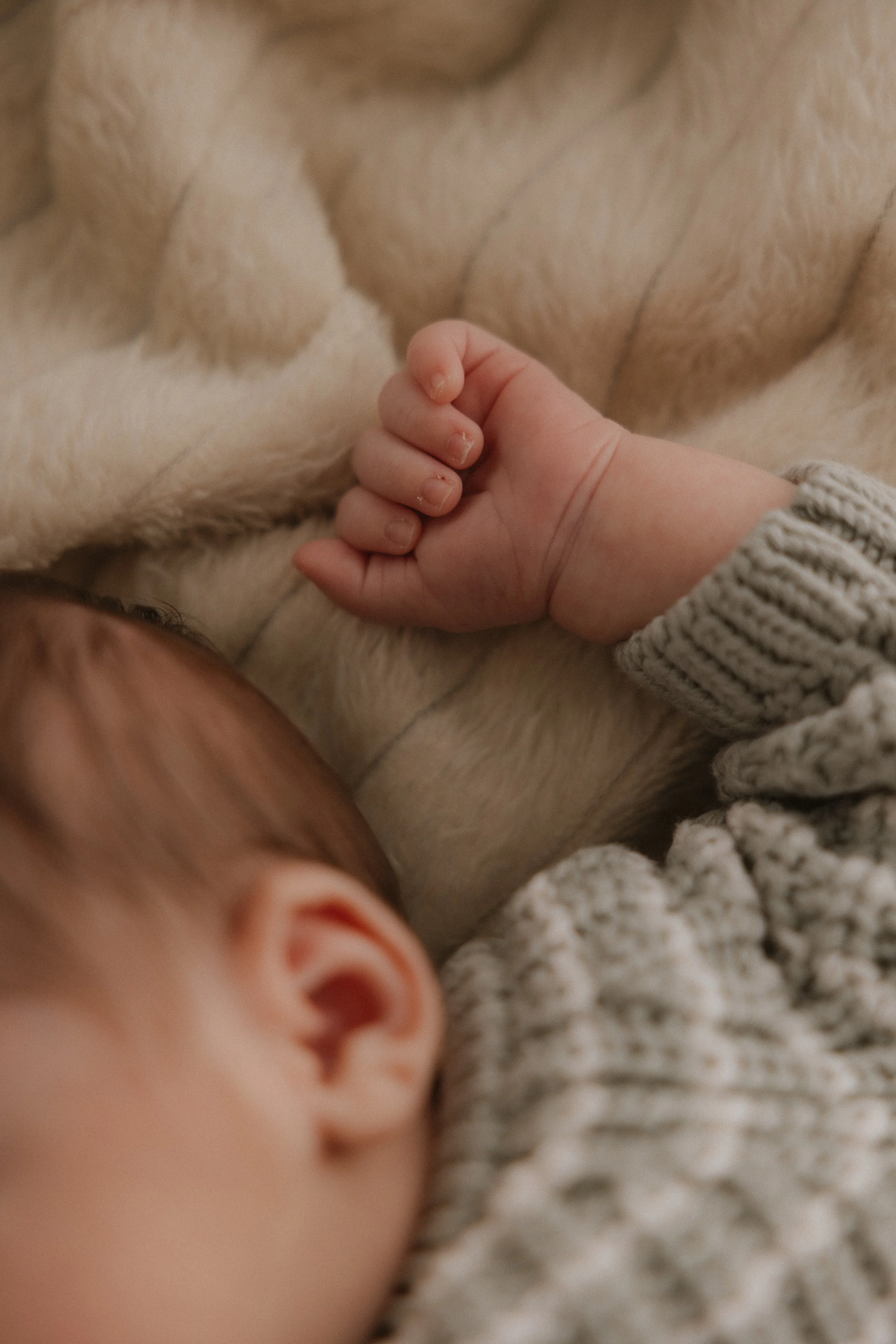 Nahaufnahme eines schlafenden Babys, das eine handgemachte Strickjacke trägt, auf einer kuscheligen Decke.