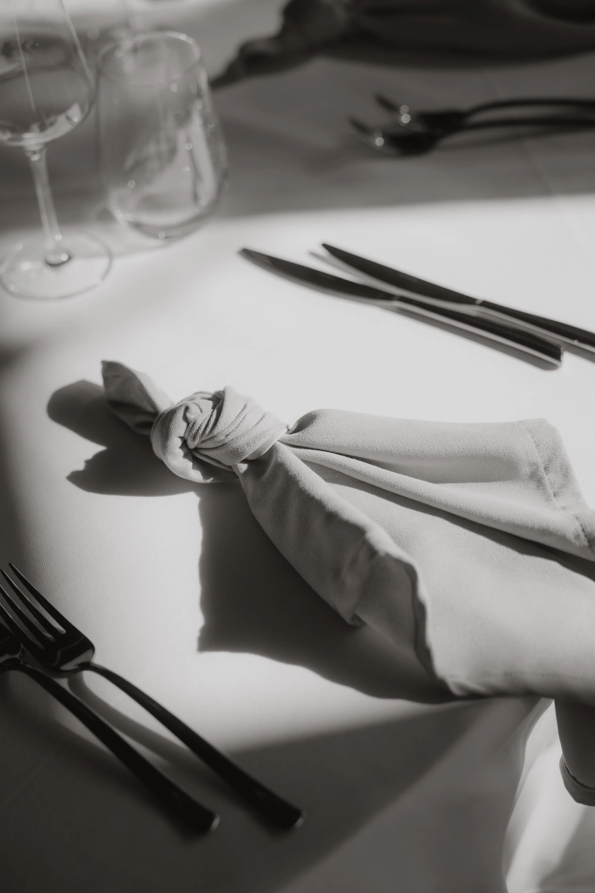 Eleganter gedeckter Tisch mit Wein- und Wassergläsern, Besteck, weißen Stoffservietten, die kunstvoll auf einem weißen Tisch platziert sind. Moderne Fotografie in der Eventschneiderei, Rottweil.