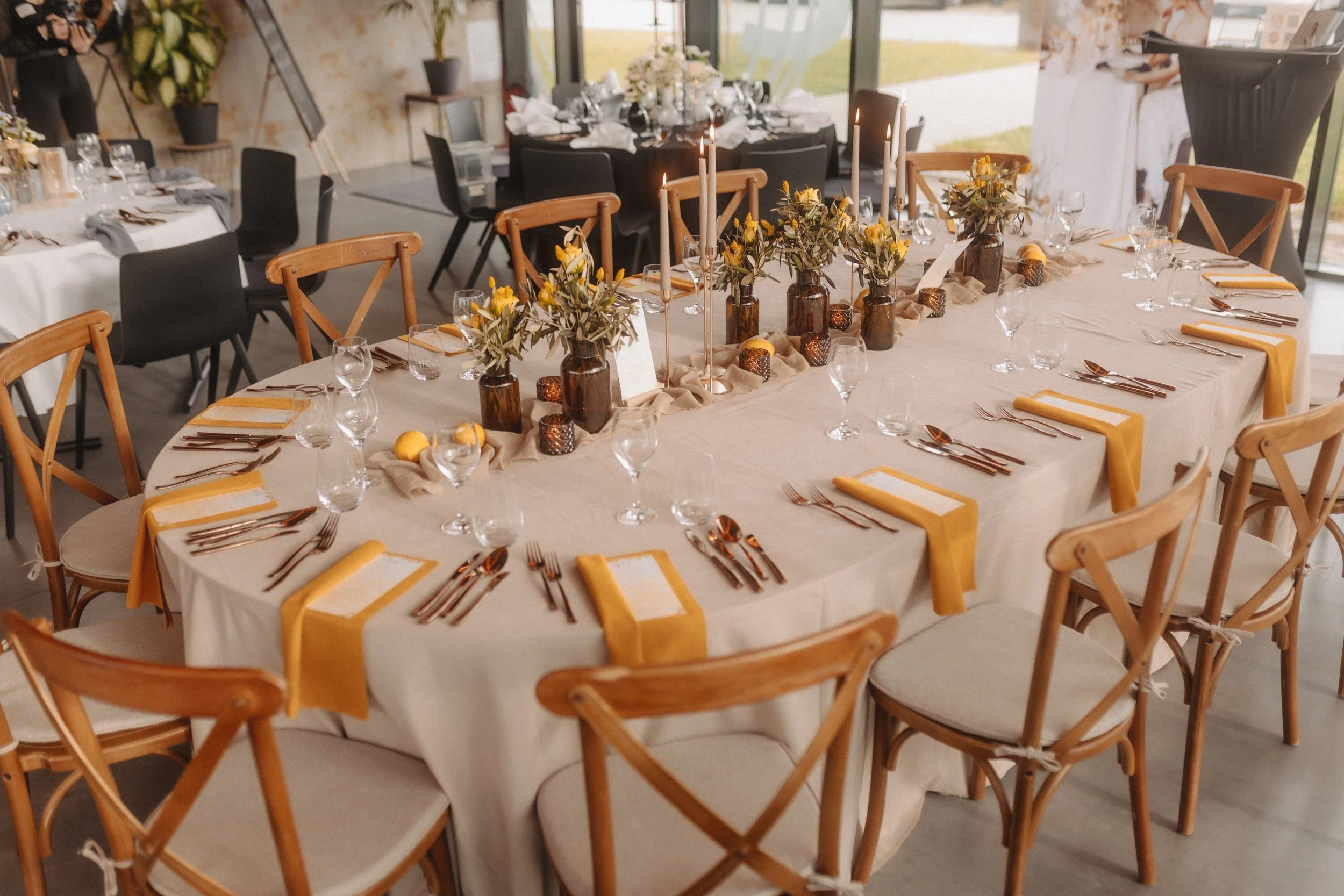 Ein festlich gedeckter Saal mit einem großen runden Tisch, dekoriert mit Blumenvasen, Kerzen, Besteck, Gläsern und Stoffservietten als Inspiration für Hochzeitsdeko. Indekoristik hat die Dekoration gemacht, Pia Heim fotografiert.