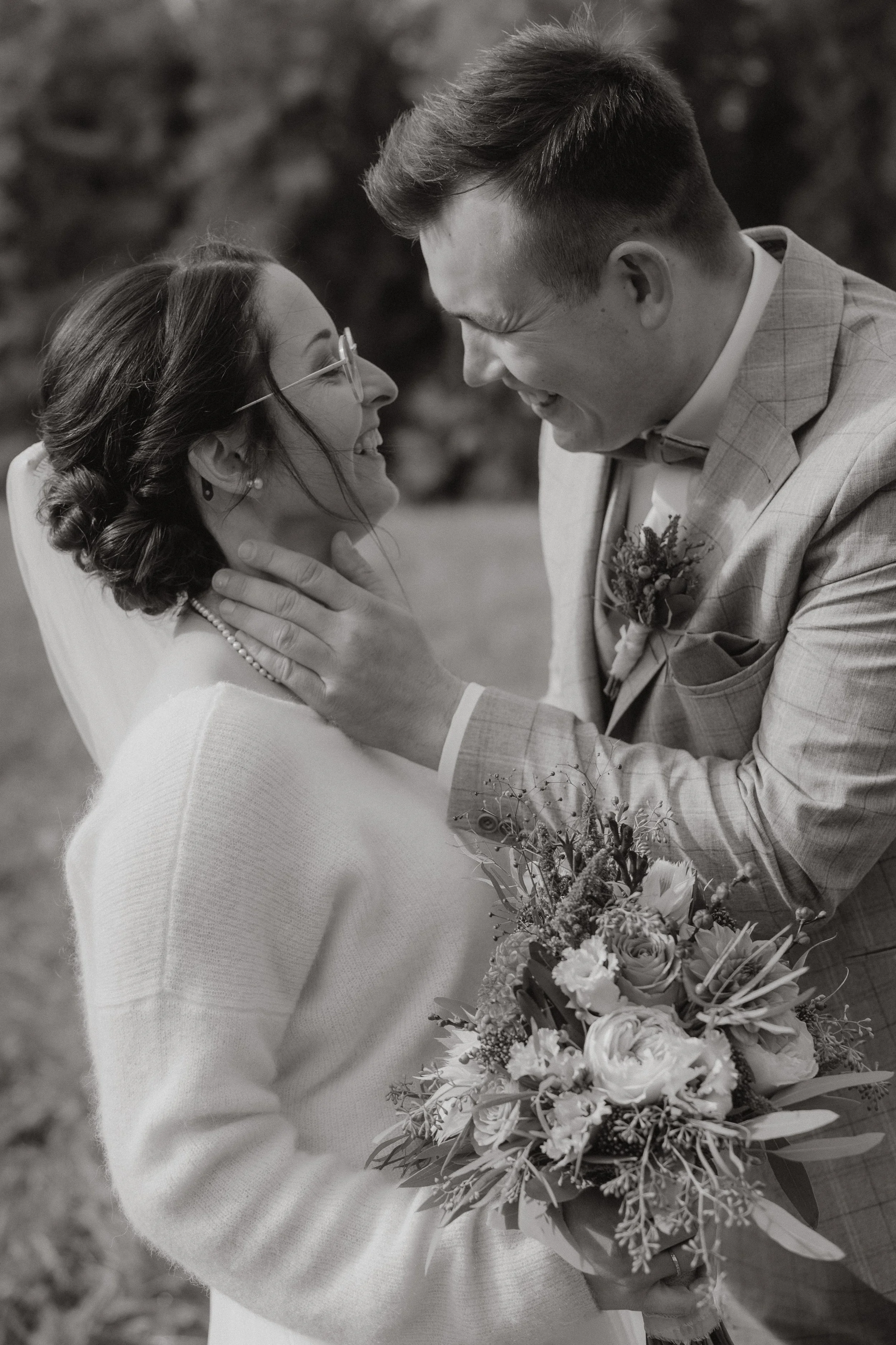 Ein glückliches Brautpaar bei einer Hochzeit, umarmt sich, der Bräutigam hält die Braut im Arm, sie hält einen Blumenstrauß, im schwarzen und weißen Foto