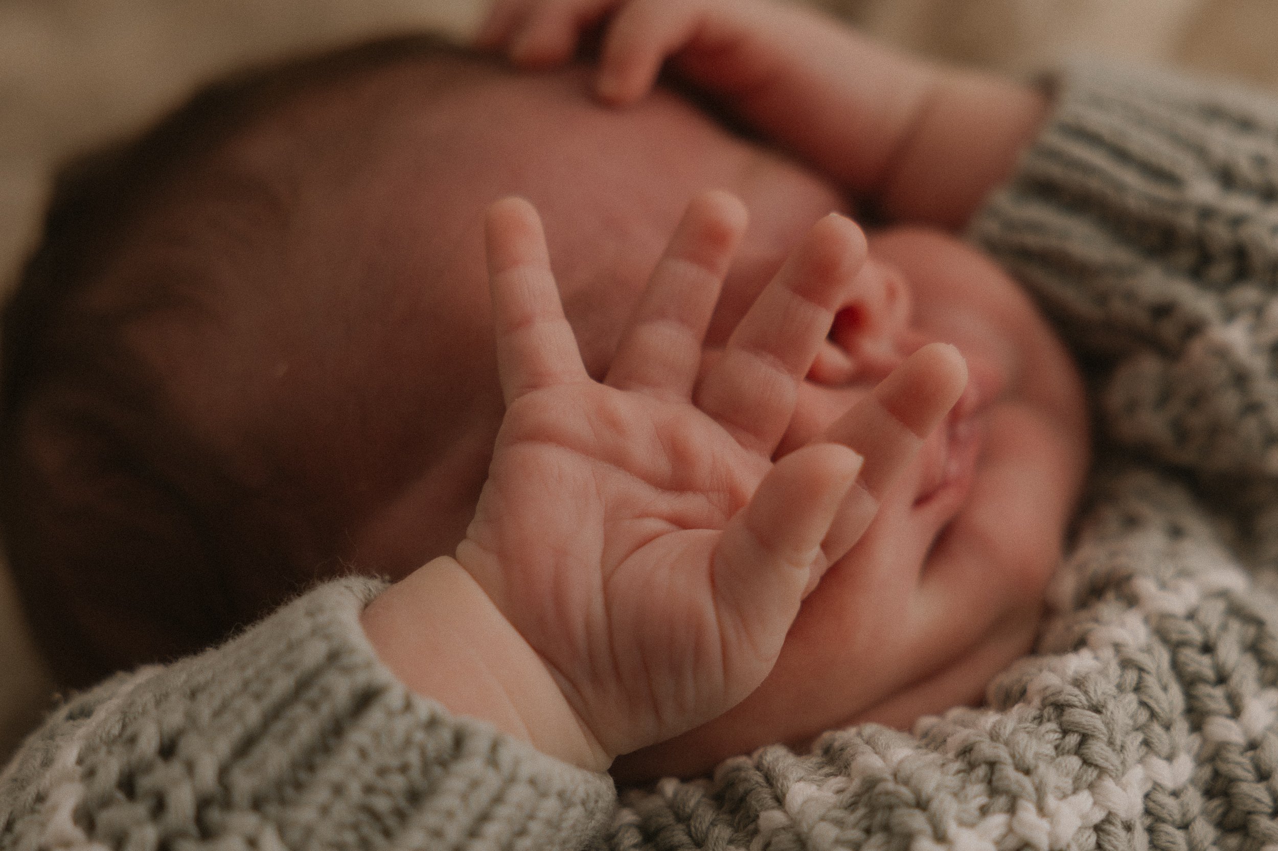 Nahaufnahme eines schlafenden Babys mit einer Hand, die eine Geste macht, während es in einem gestrickten Pullover liegt.