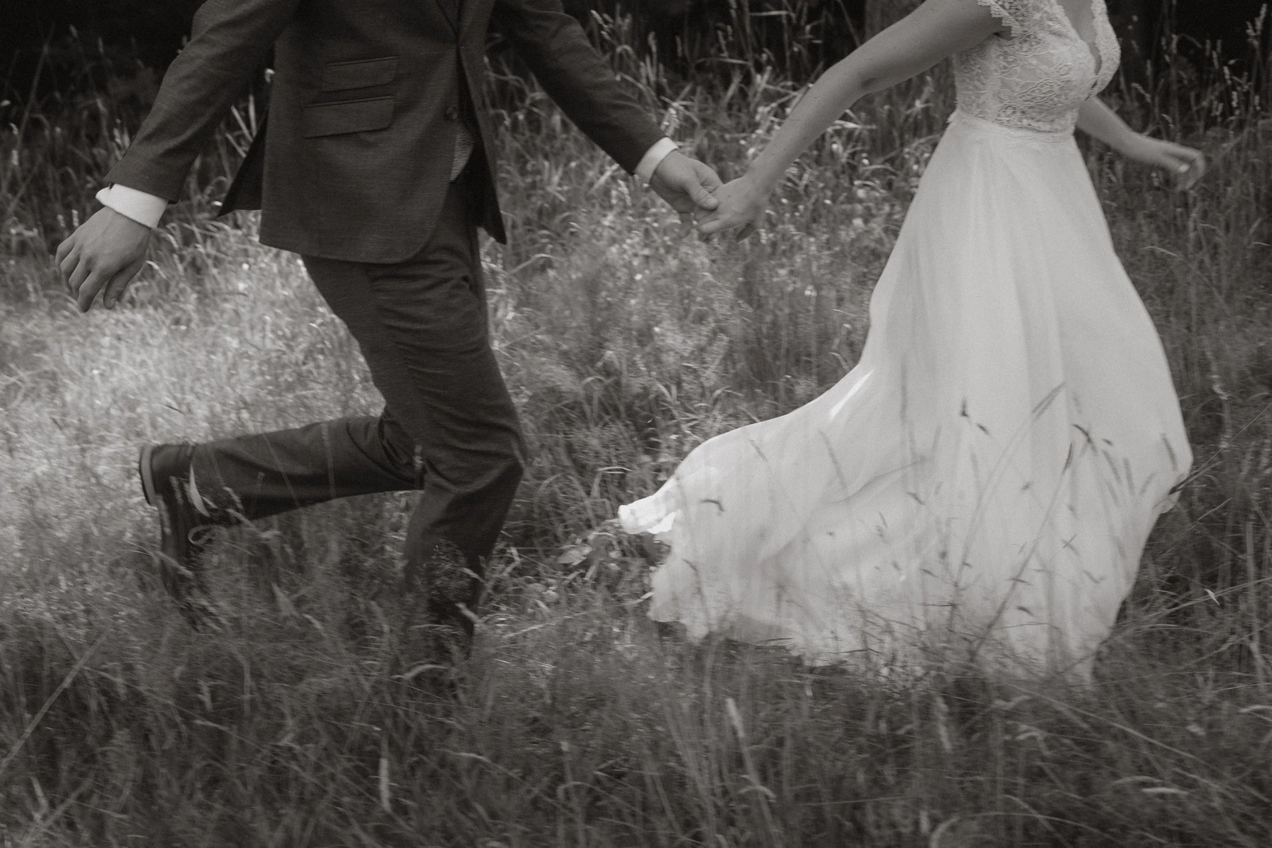 Ein Paar läuft Hand in Hand durch ein Grasefeld, das Bild ist schwarz-weiß. Slowshutter Fotografie mit dem Hochzeitsfotograf in Rottweil.