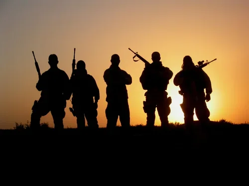 Silhouettes of five soldiers holding rifles against a sunset background.