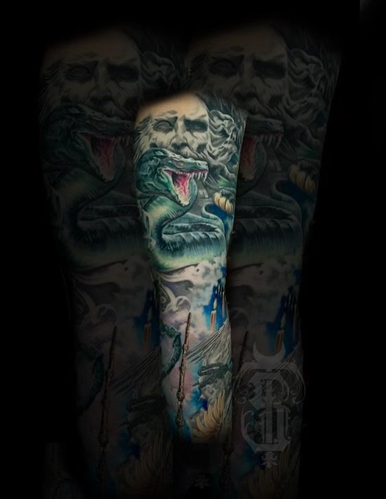 Colorful tattoos on a person's arm and chest, featuring a lion with an open mouth and a snake, with various other designs and symbols.