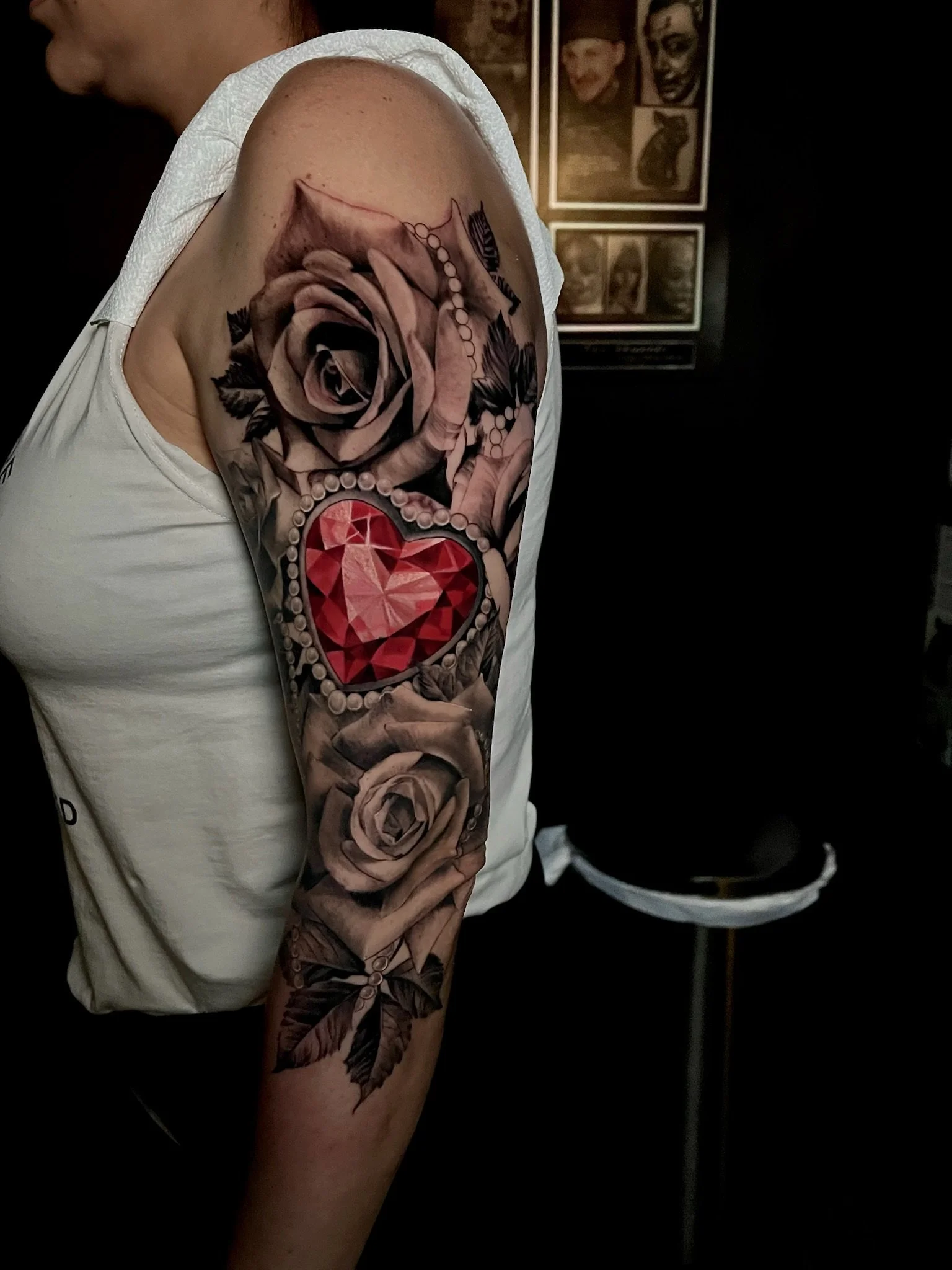 Tattoo of roses, hands and a red gemstone on a person's upper arm.