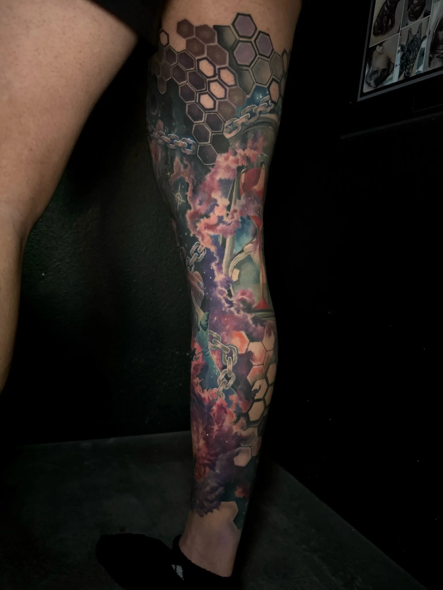 Colorful tattoo sleeve featuring a galaxy sky, pink clouds, chain links, honeycomb pattern, and digital art elements on a person's arm.
