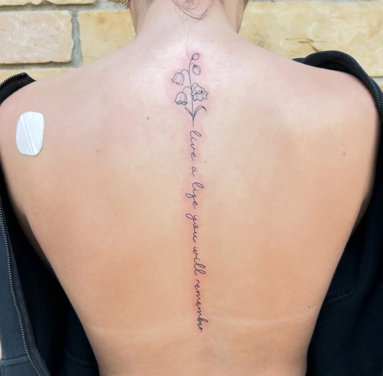 Back of a person with a tattoo of a flower and the words 'live a life you will remember' written in cursive.