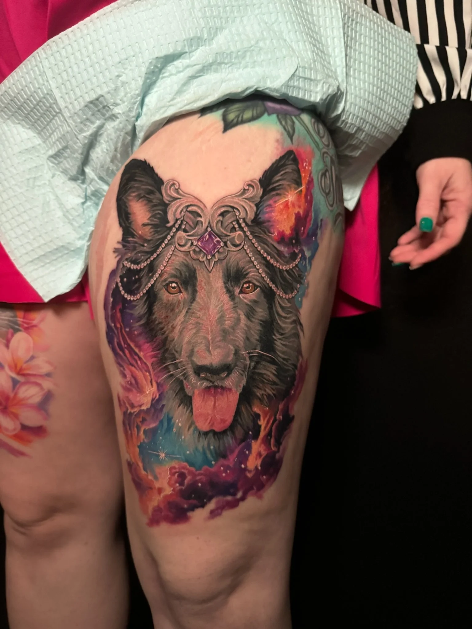 Colorful tattoo of a wolf with a gemstone headpiece on a person's thigh, surrounded by vibrant nebula-like clouds and stars.