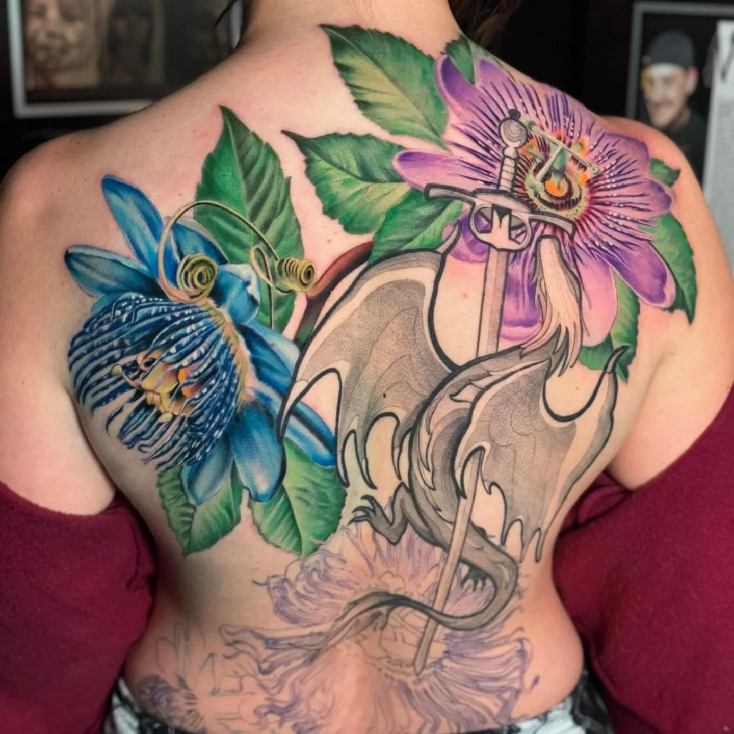 Colorful tattoo of blue butterfly and purple flower with green leaves on a person's shoulder and chest.