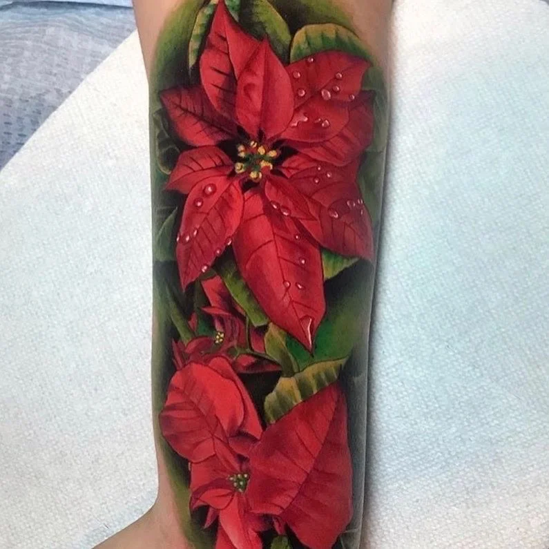Tattoo of red poinsettia flowers with green leaves on a person's forearm.
