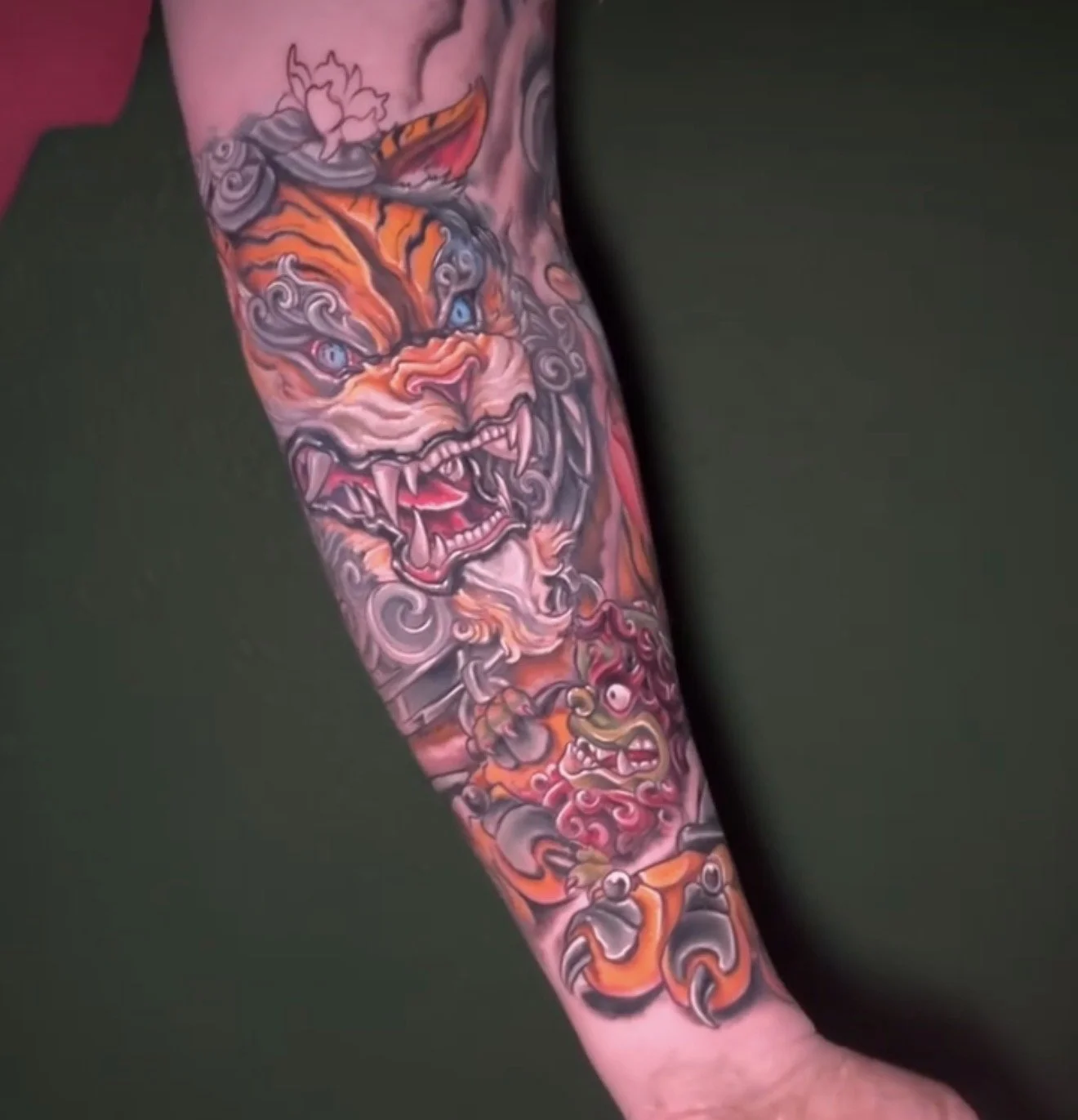 a colorful tattoo on a person's forearm of a orange japanese style tiger and red dragon with swirling details and a growling mouth