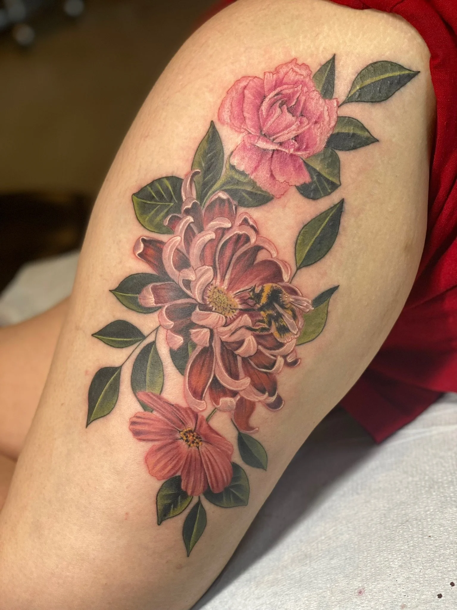 Colorful floral tattoo featuring pink roses, petals, and green leaves on person's upper arm.