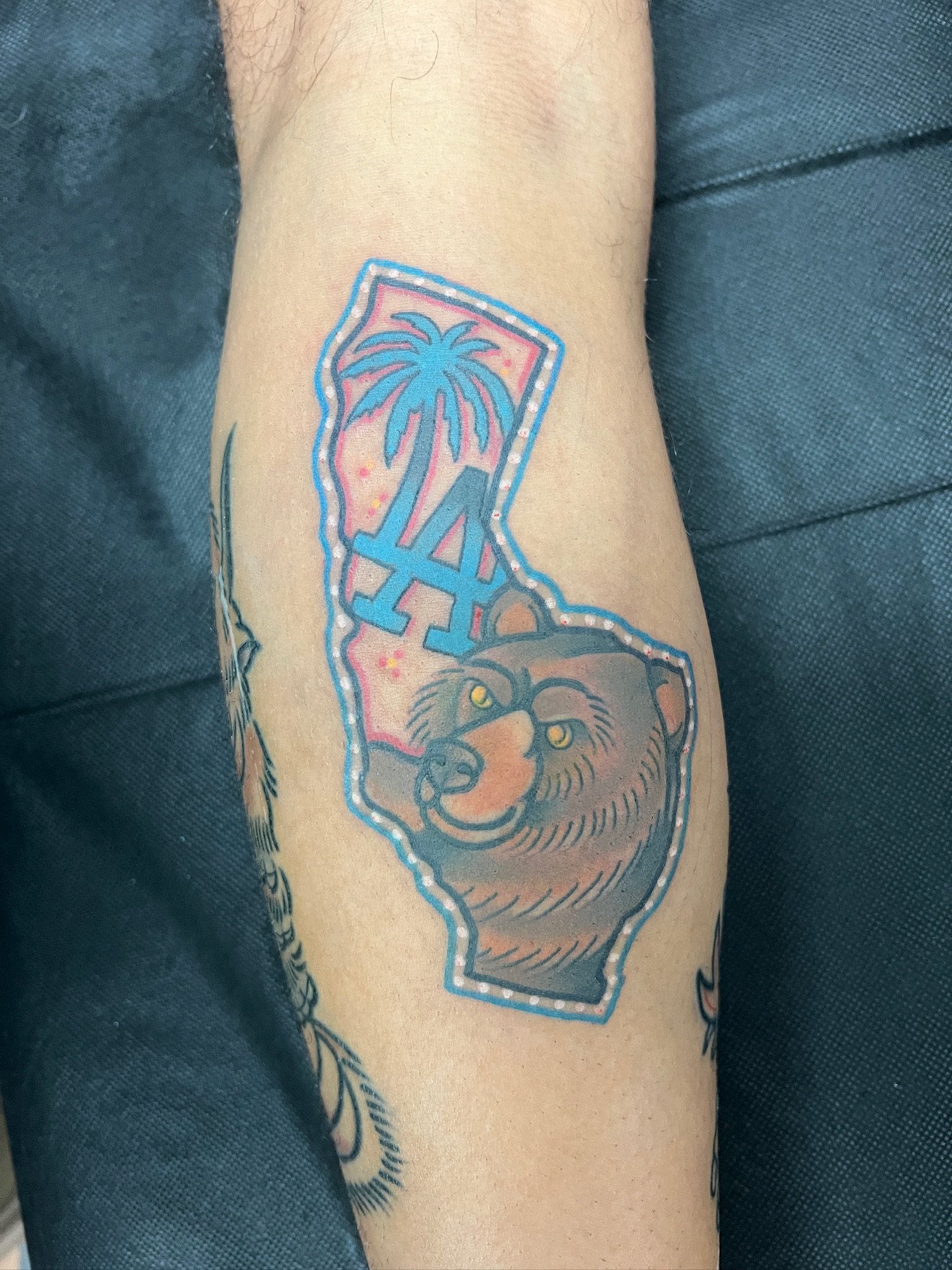 Tattoo of the state of California with a palm tree, LA initials, and a bear's face inside