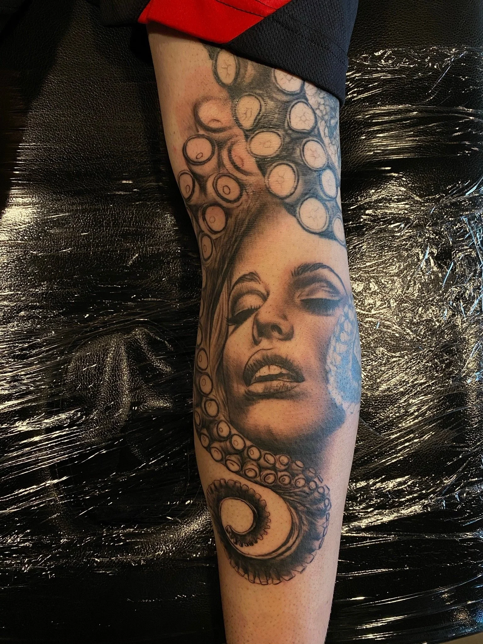 Tattoo of a woman's face with closed eyes and parted lips, intertwined with octopus tentacles on a person's arm.