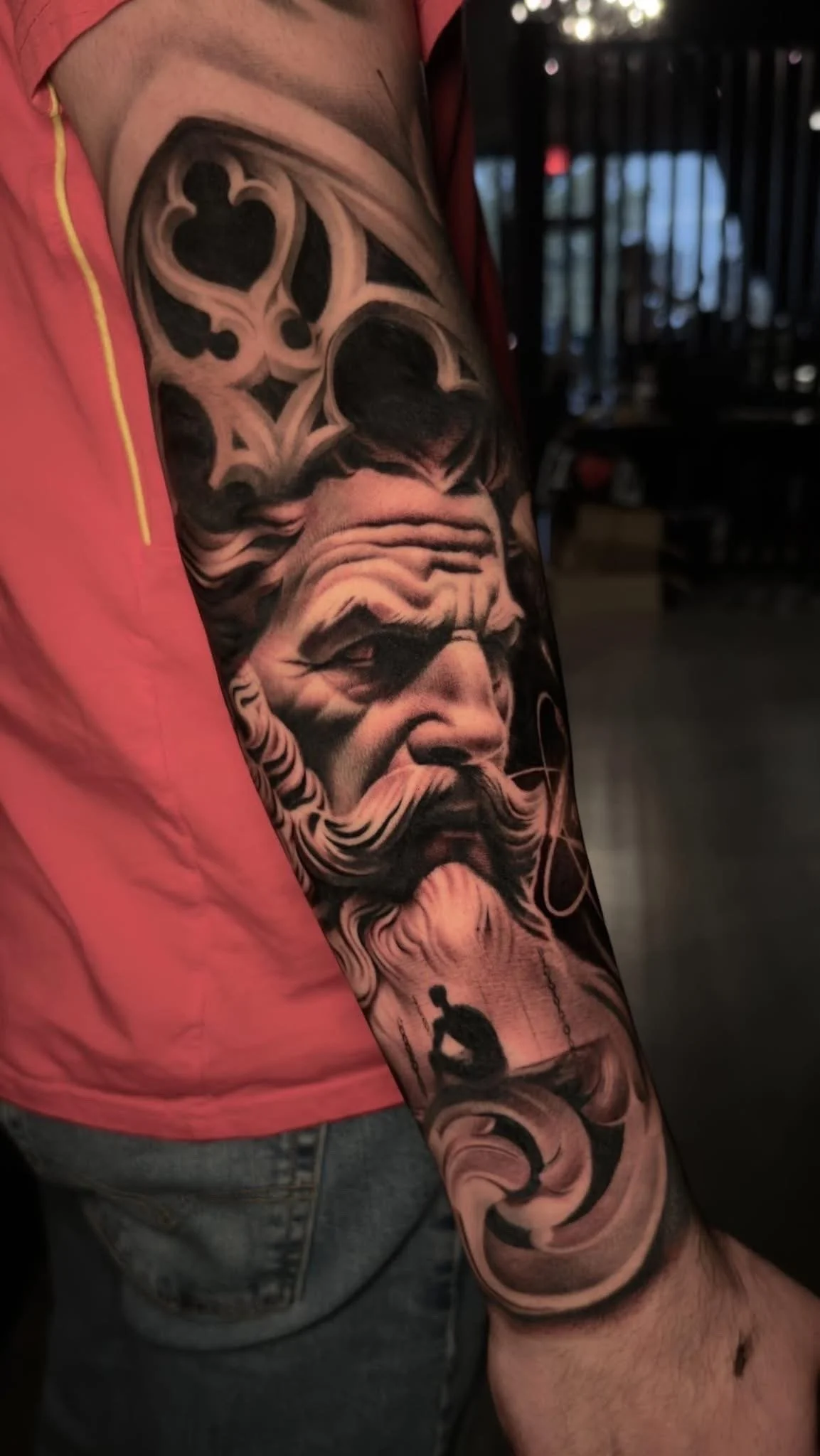 Black and gray tattoo sleeve featuring a bearded man with long hair, floral designs, a person sitting on a swing, and abstract elements.
