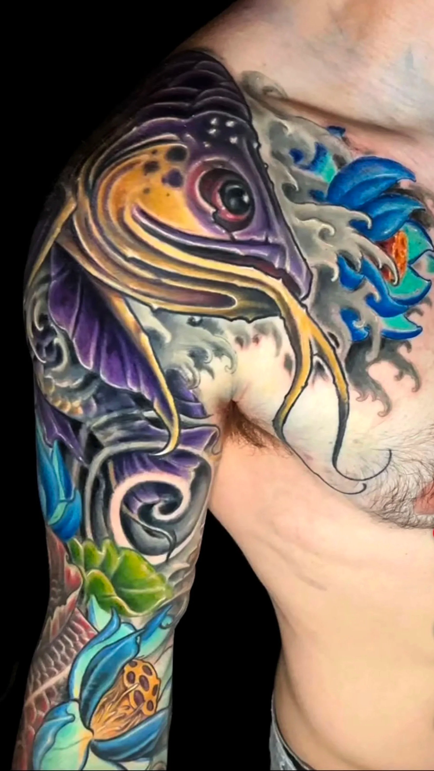 Colorful tattoo of a fish with vibrant colors and detailed shading, covering the person's upper arm and shoulder.