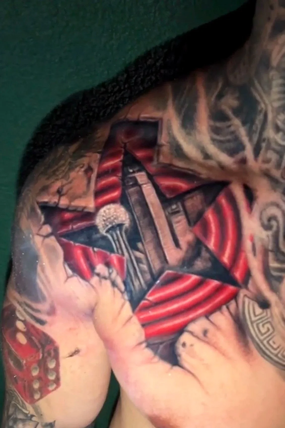 Close-up of a person's shoulder and chest tattoo featuring a detailed skyline with red and black colors, and biological elements like veins and muscles.