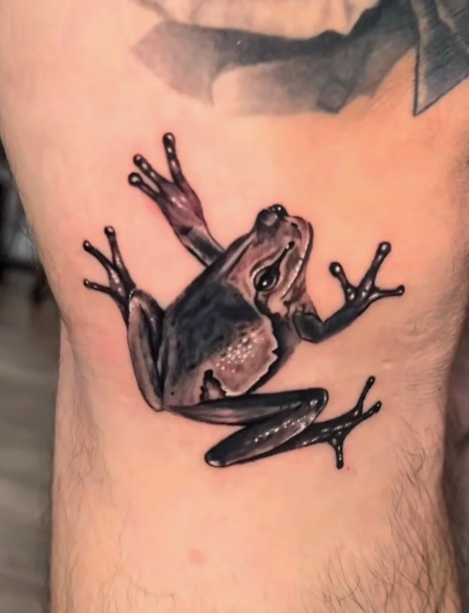 Tattoo of a frog climbing on a person's skin, depicting detailed shading and realistic features.
