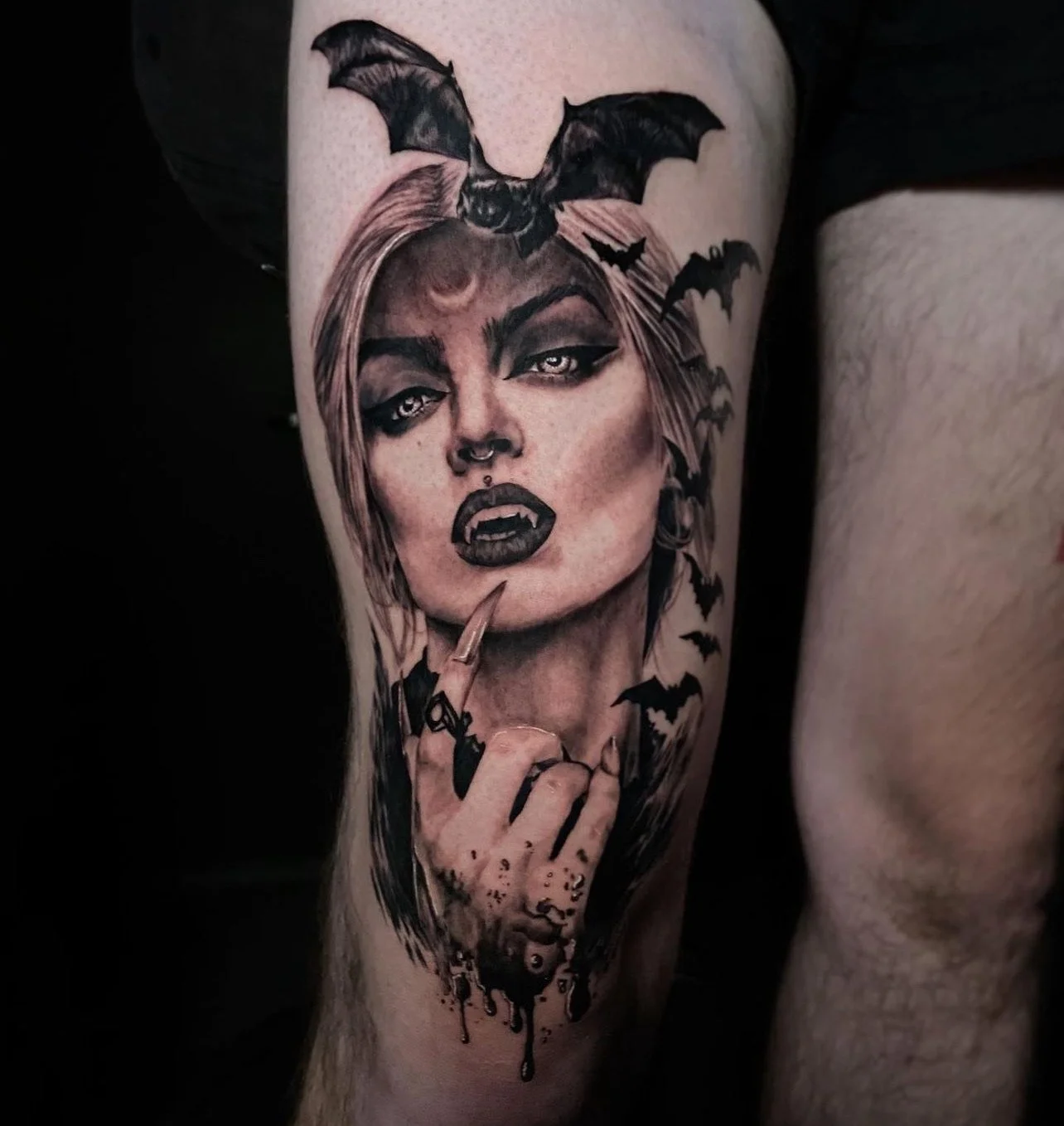 Black and gray portrait tattoo of a woman with short hair, vampire fangs, and dark makeup, surrounded by flying bats.