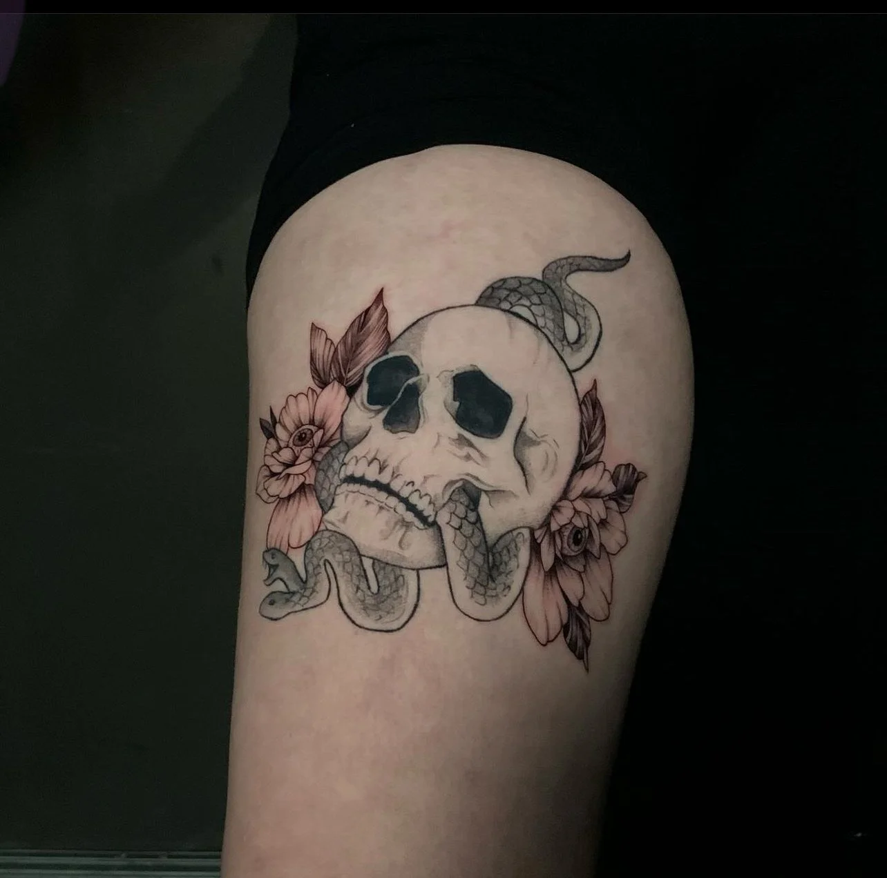 Tattoo of a skull with a snake wrapped around it and flowers around the skull.