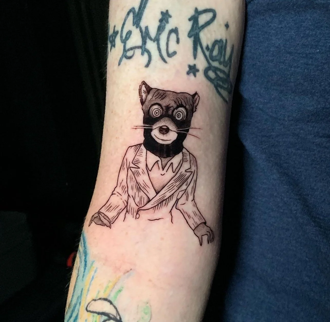 Tattoo of a raccoon with hypnotic eyes wearing a suit.