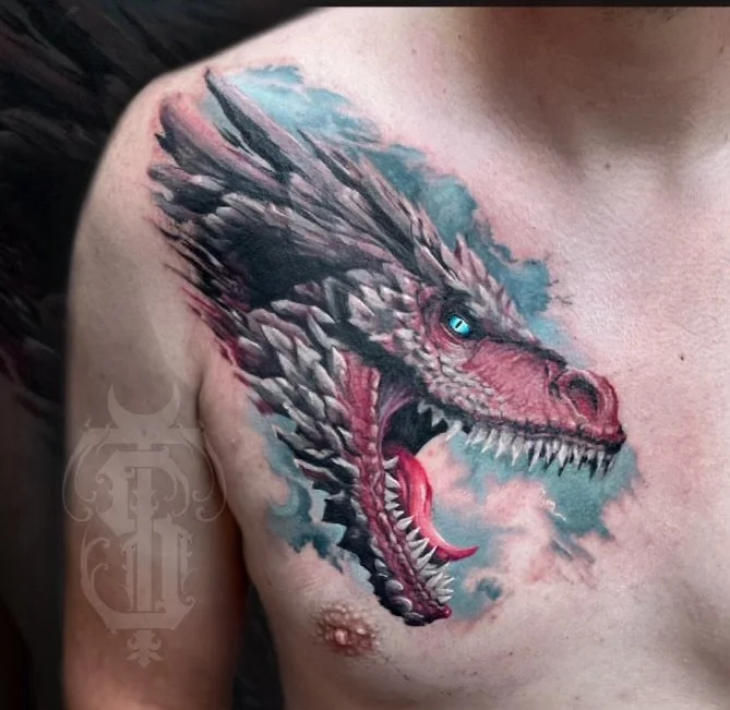 Close-up of a person's chest with a detailed dragon tattoo featuring a fierce open-mouthed dragon with sharp teeth, blue eye, and pink accents.