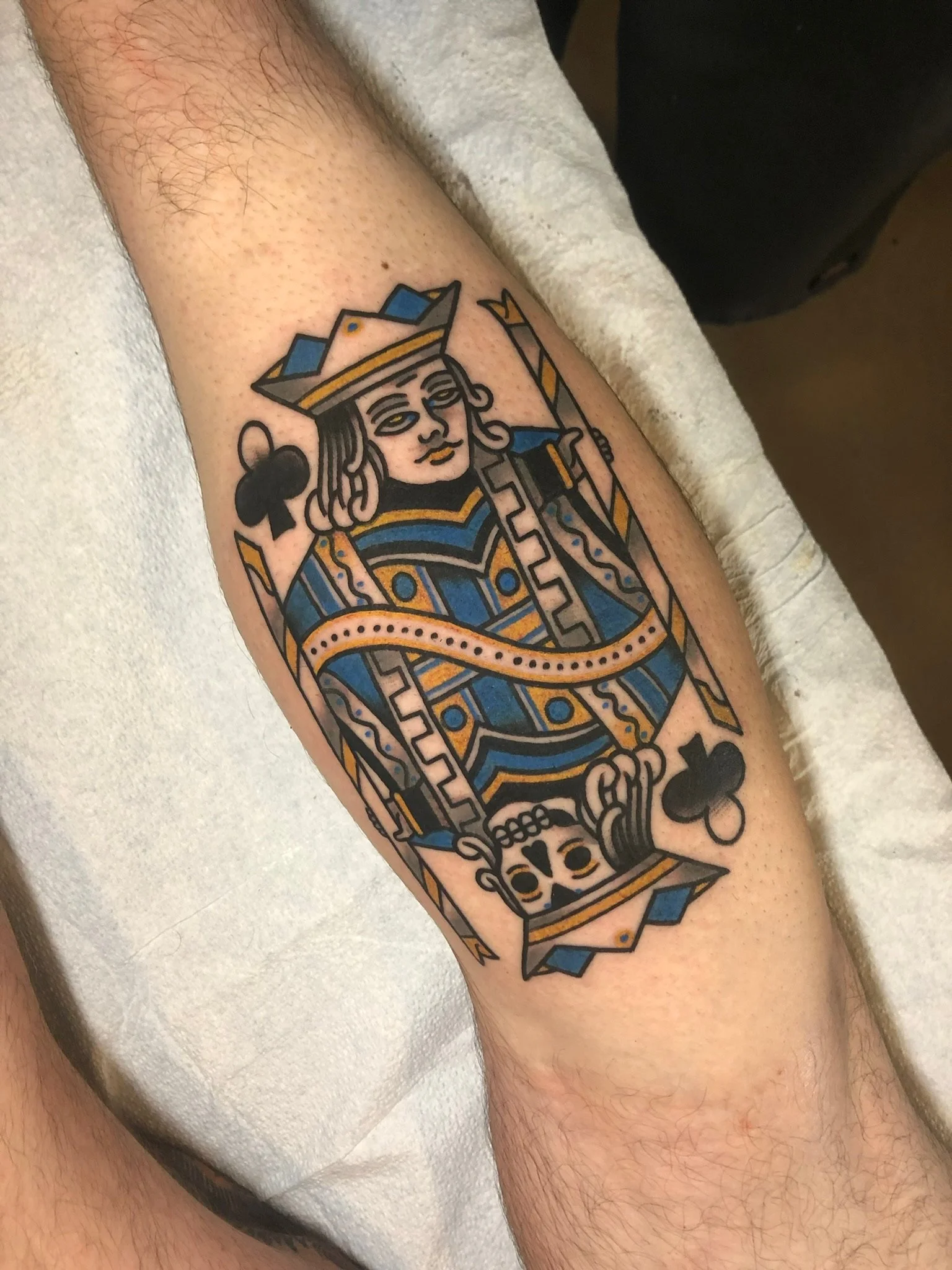 A colorful tattoo of the Queen of Clubs playing card on a person's forearm.