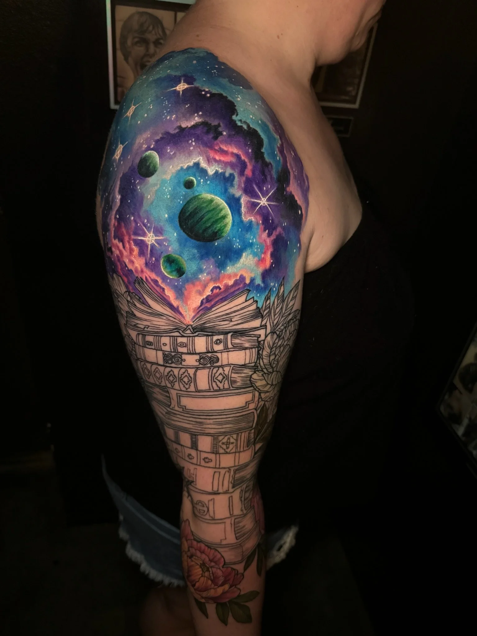 Colorful galaxy sky with planets and stars above an open book on a person's shoulder tattoo.