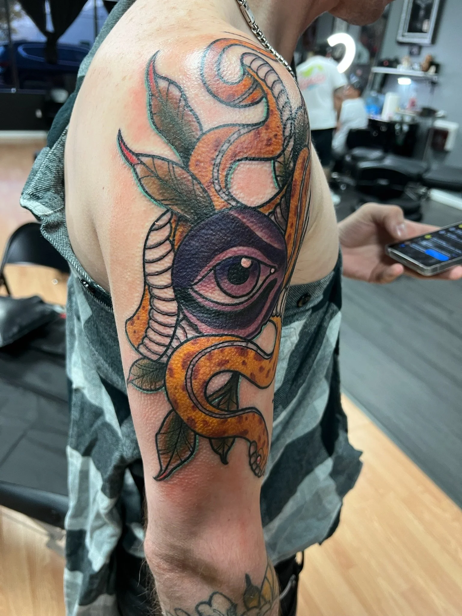 Tattoo of an eye, snake, and leaf design on a person's upper arm.