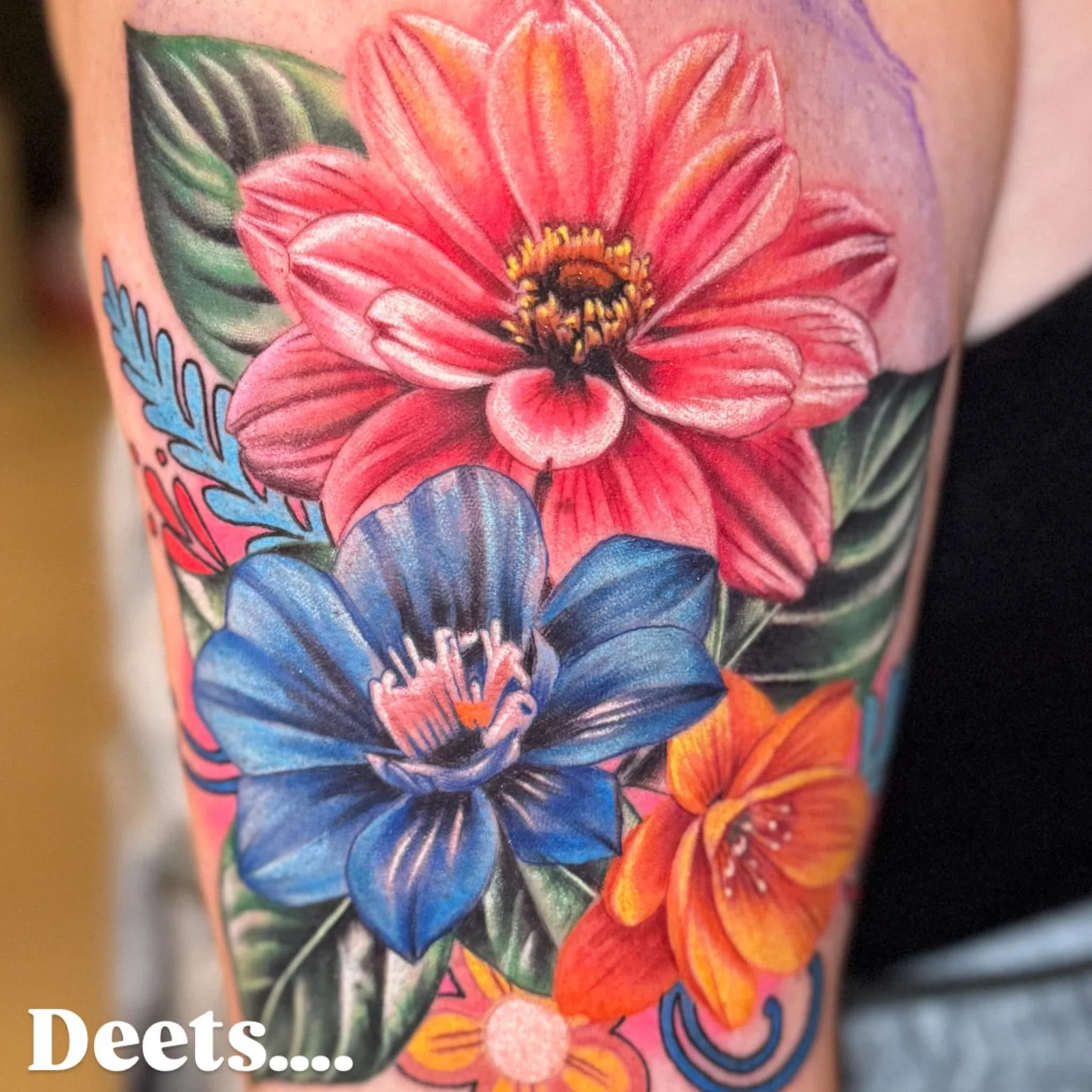 A colorful tattoo on a person's arm of pink and orange flowers with green leaves and blue accents.