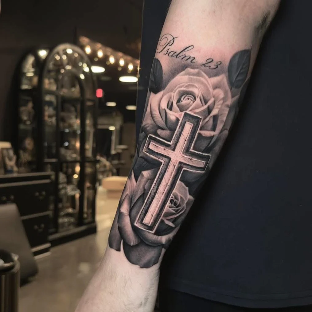 A tattoo on a person's arm featuring a cross, a rose, and the words 'Psalm 23' in script.