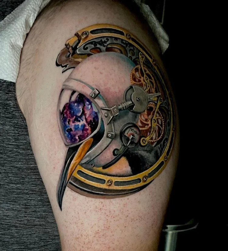 Tattoo of a mechanical watch with gears and a galaxy inside the watch face on a person's upper arm.
